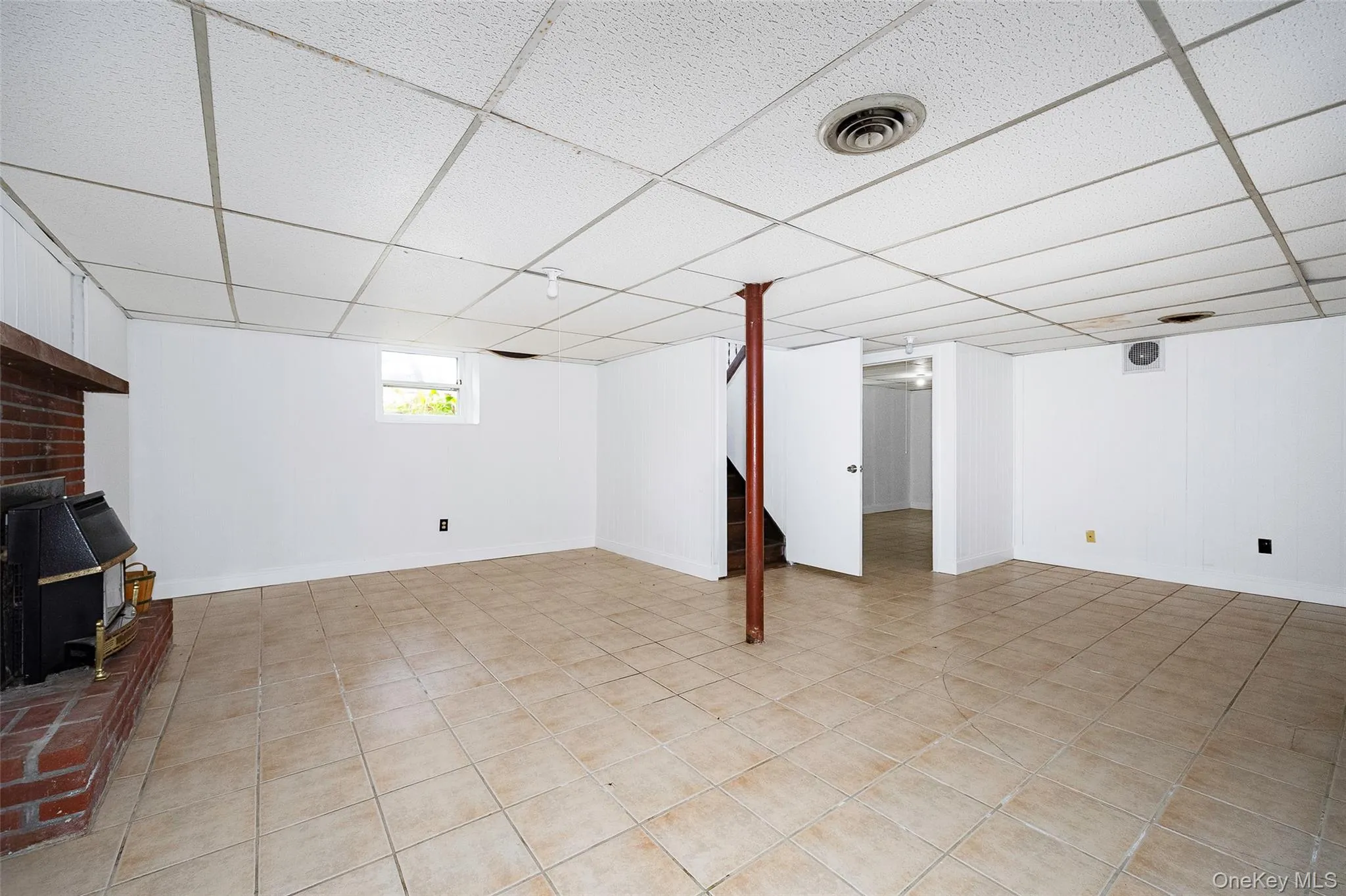 Basement featuring a paneled ceiling, a wood stove, and light tile patterned floors Basement featuring a paneled ceiling, a wood stove, and light tile patterned floors