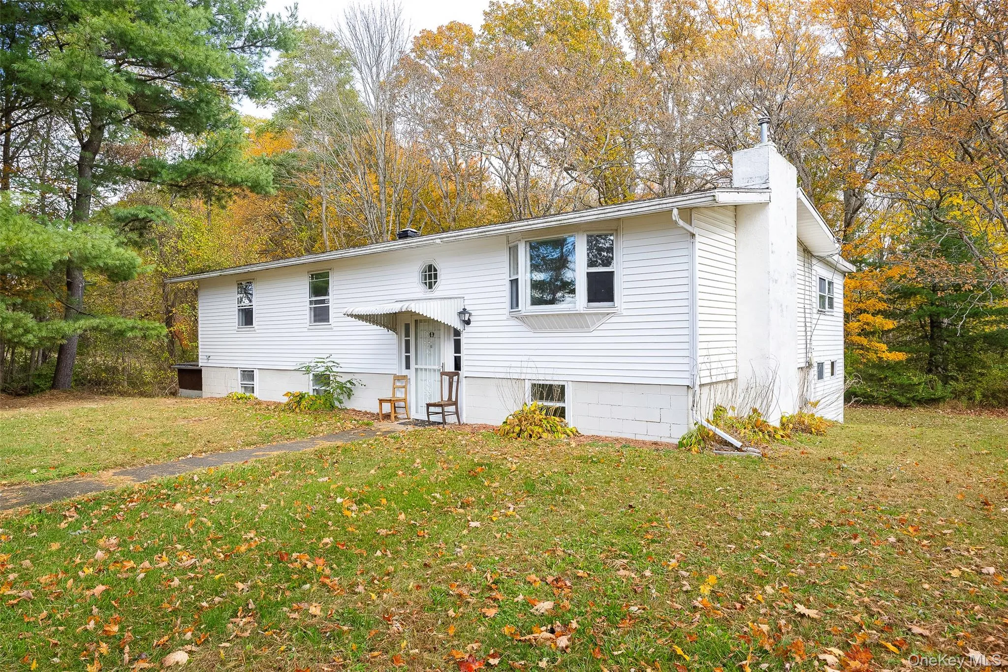 Bi-level home featuring a front lawn, a chimney, and view of scattered trees Bi-level home featuring a front lawn, a chimney, and view of scattered trees