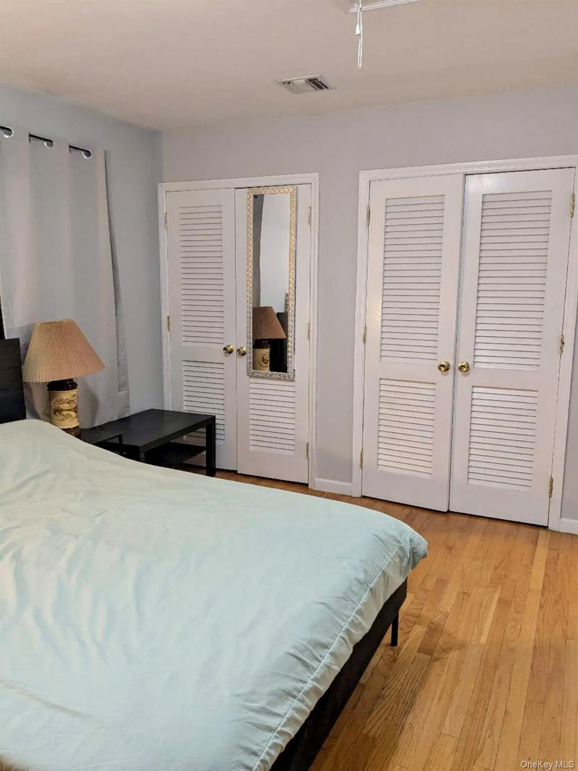 Bedroom featuring wood-finish flooring, light gray walls, and two sets of louvered bifold closet doors Bedroom featuring wood-finish flooring, light gray walls, and two sets of louvered bifold closet doors