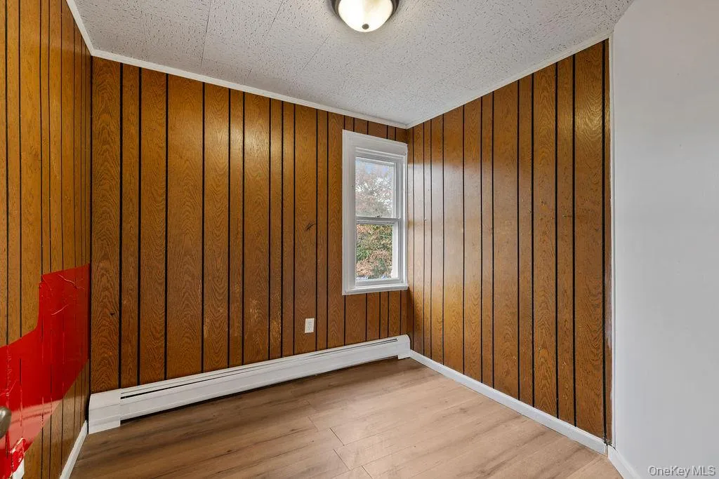 Empty room featuring ornamental molding, baseboard heating, and wooden walls Empty room featuring ornamental molding, baseboard heating, and wooden walls