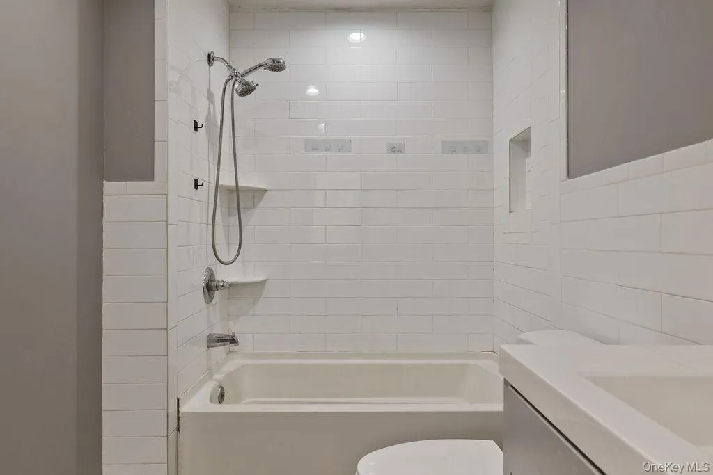 Full bathroom featuring tiled shower / bath combo, toilet, tile walls, and vanity Full bathroom featuring tiled shower / bath combo, toilet, tile walls, and vanity