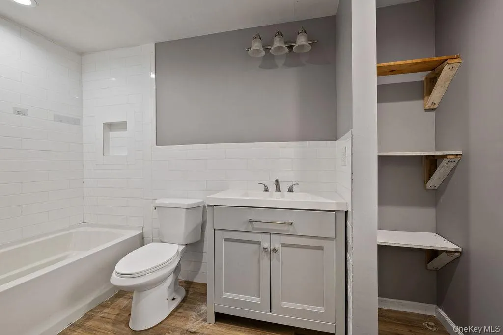 Full bathroom with vanity, hardwood / wood-style floors, toilet, shower / bathing tub combination, and tile walls Full bathroom with vanity, hardwood / wood-style floors, toilet, shower / bathing tub combination, and tile walls
