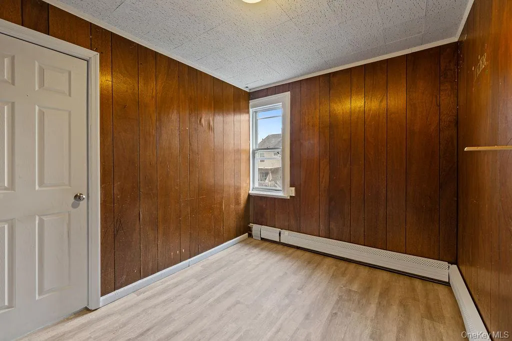 Empty room with wood walls, light hardwood / wood-style floors, and baseboard heating Empty room with wood walls, light hardwood / wood-style floors, and baseboard heating