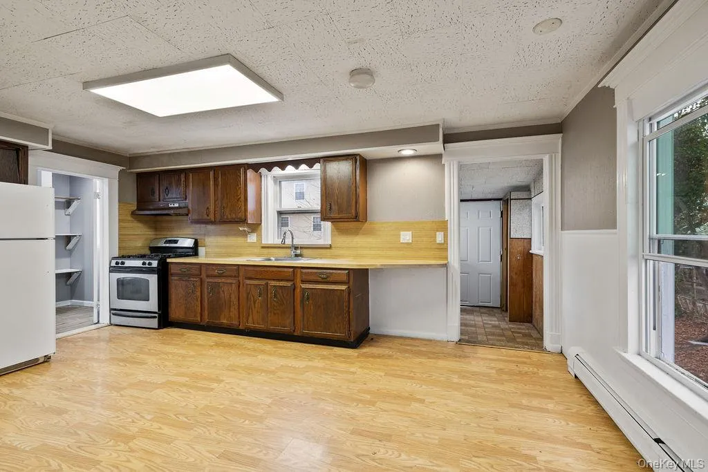 Kitchen featuring stainless steel gas range, baseboard heating, range hood, white refrigerator, and decorative backsplash Kitchen featuring stainless steel gas range, baseboard heating, range hood, white refrigerator, and decorative backsplash
