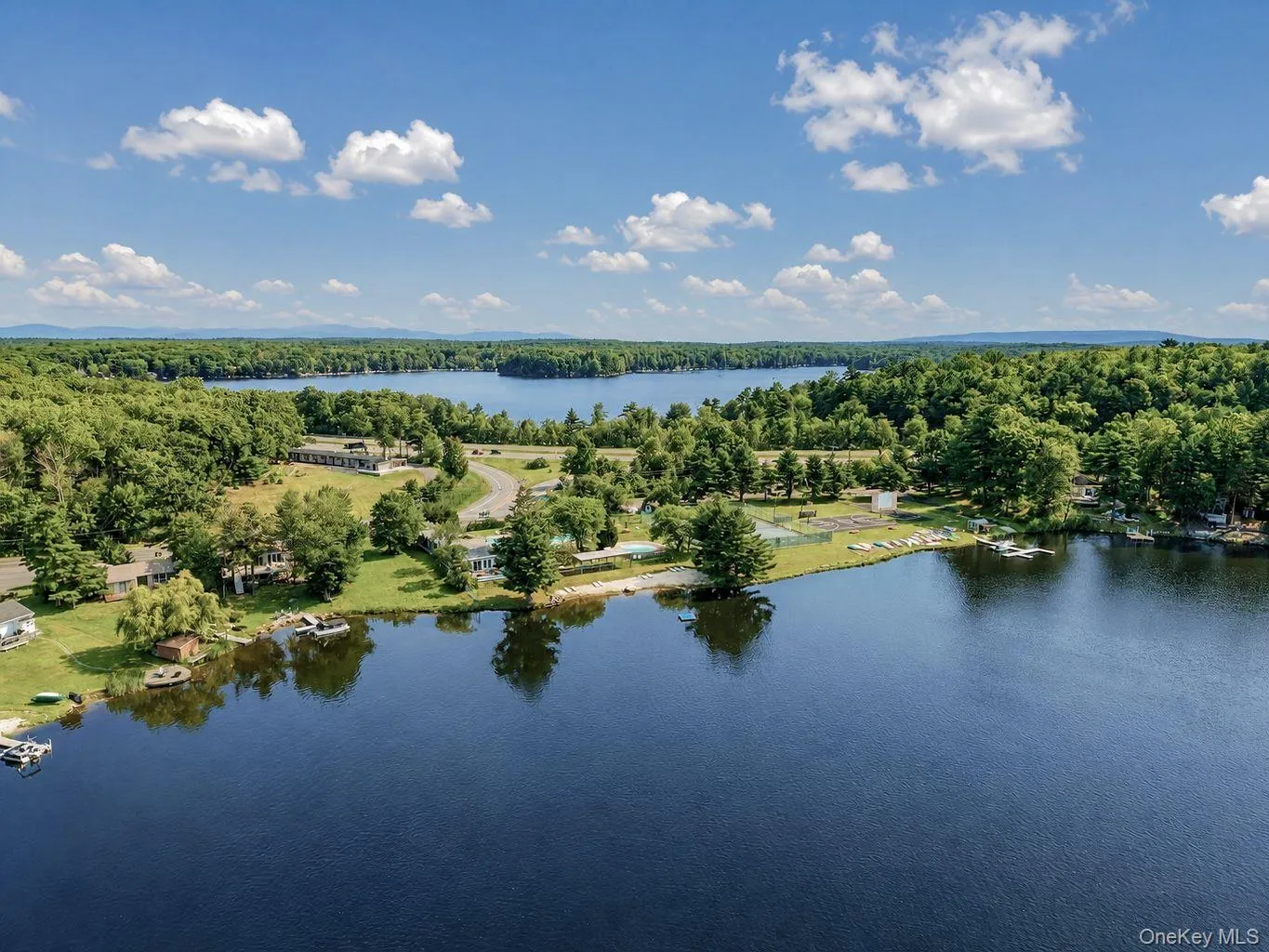 Expansive waterfront property featuring a substantial body of water, lush green tree lines, distant rolling hills, multiple docks, and a sandy beach area Expansive waterfront property featuring a substantial body of water, lush green tree lines, distant rolling hills, multiple docks, and a sandy beach area