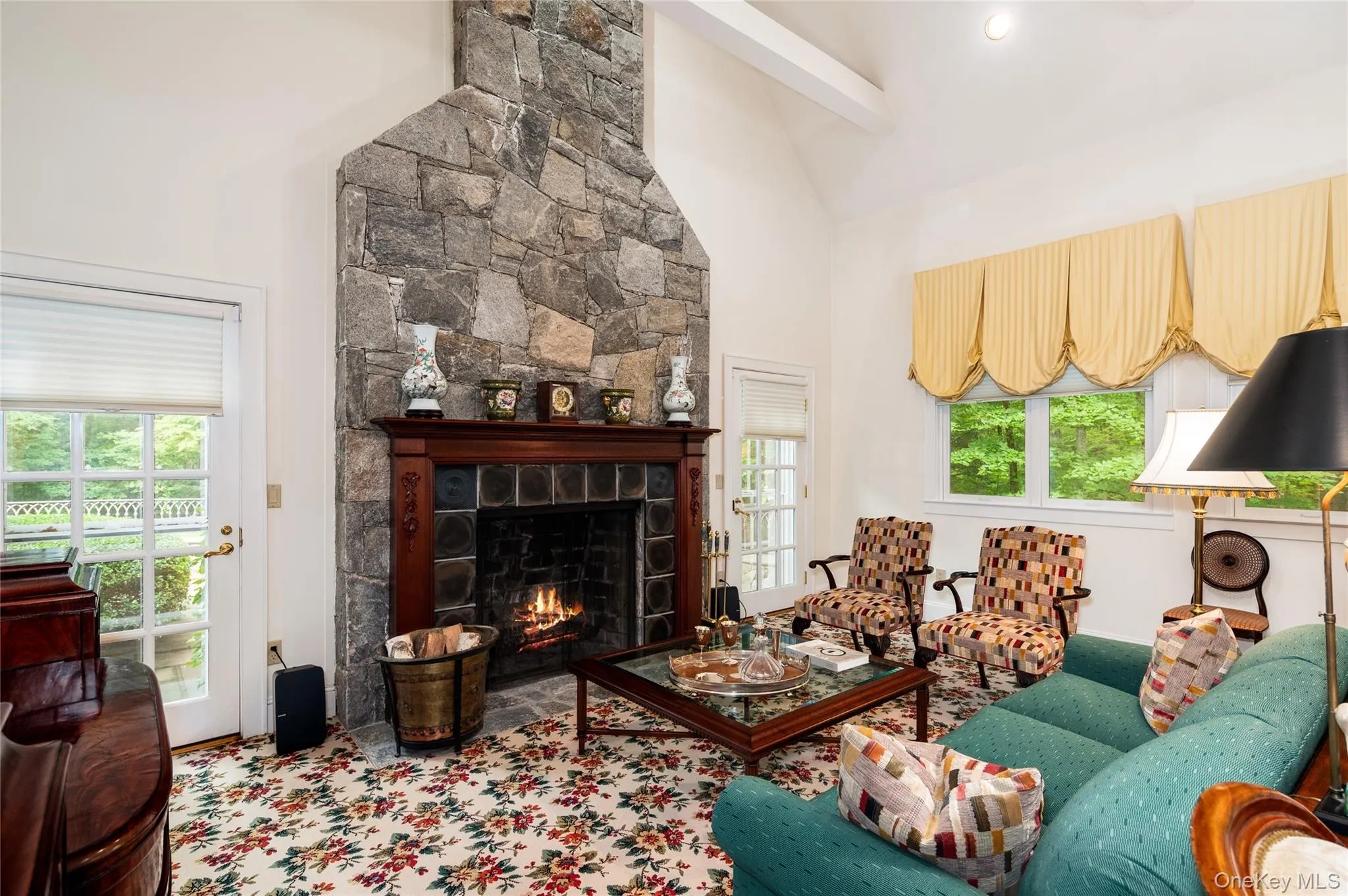 The fireplace anchors the room, flanked by doors to access an additional patio, vaulted ceiling with beams. The fireplace anchors the room, flanked by doors to access an additional patio, vaulted ceiling with beams.