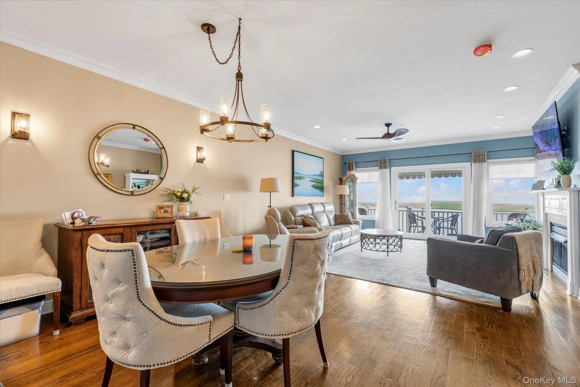 Open concept living and dining area featuring wood-finish flooring, a contemporary ceiling fan, and a fireplace with a white mantel Open concept living and dining area featuring wood-finish flooring, a contemporary ceiling fan, and a fireplace with a white mantel