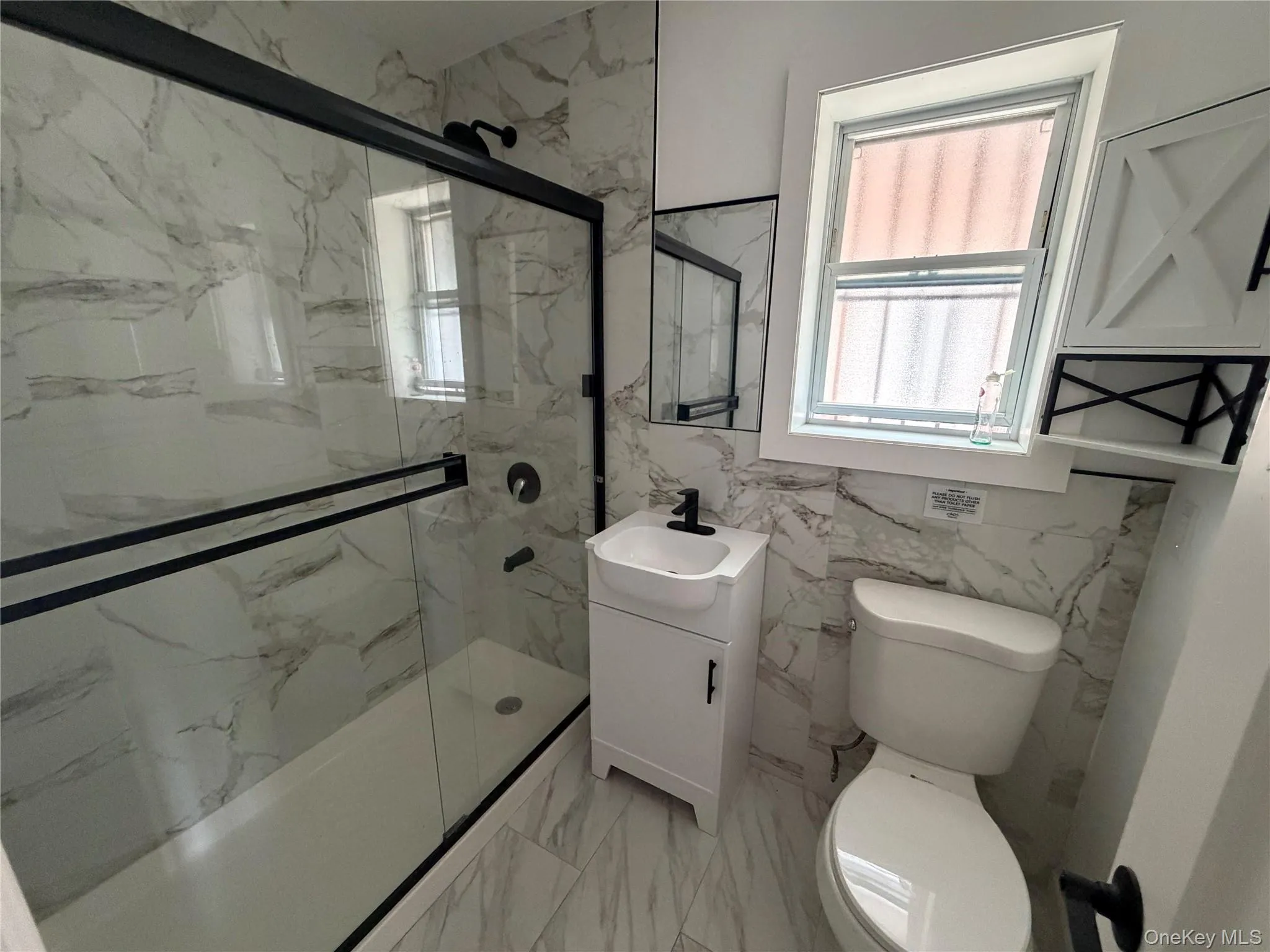 Contemporary bathroom featuring a walk-in shower with black-framed glass enclosure, white marble-look wall and floor tiling, and a modern vanity with integrated sink Contemporary bathroom featuring a walk-in shower with black-framed glass enclosure, white marble-look wall and floor tiling, and a modern vanity with integrated sink