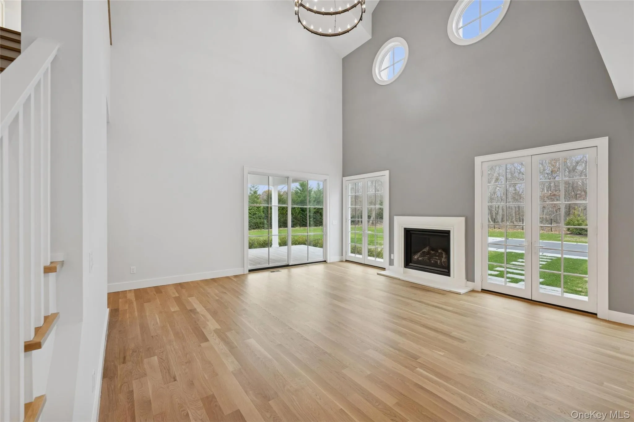 Living room featuring healthy amount of natural light, light wood finished floors, a glass covered fireplace, a chandelier, and a towering ceiling Living room featuring healthy amount of natural light, light wood finished floors, a glass covered fireplace, a chandelier, and a towering ceiling