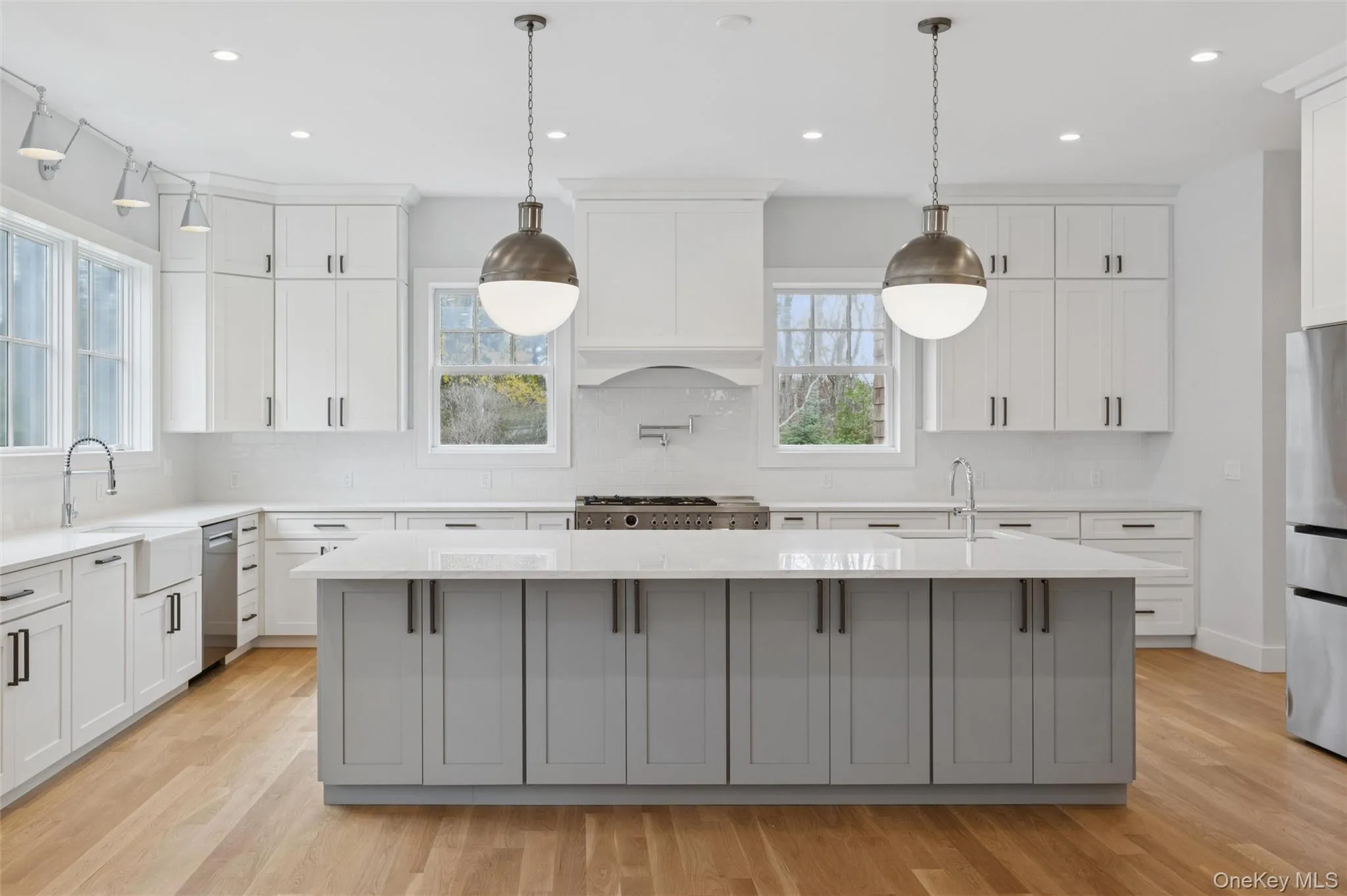 Kitchen with a spacious island, gray cabinetry, hanging light fixtures, white cabinets, and recessed lighting Kitchen with a spacious island, gray cabinetry, hanging light fixtures, white cabinets, and recessed lighting