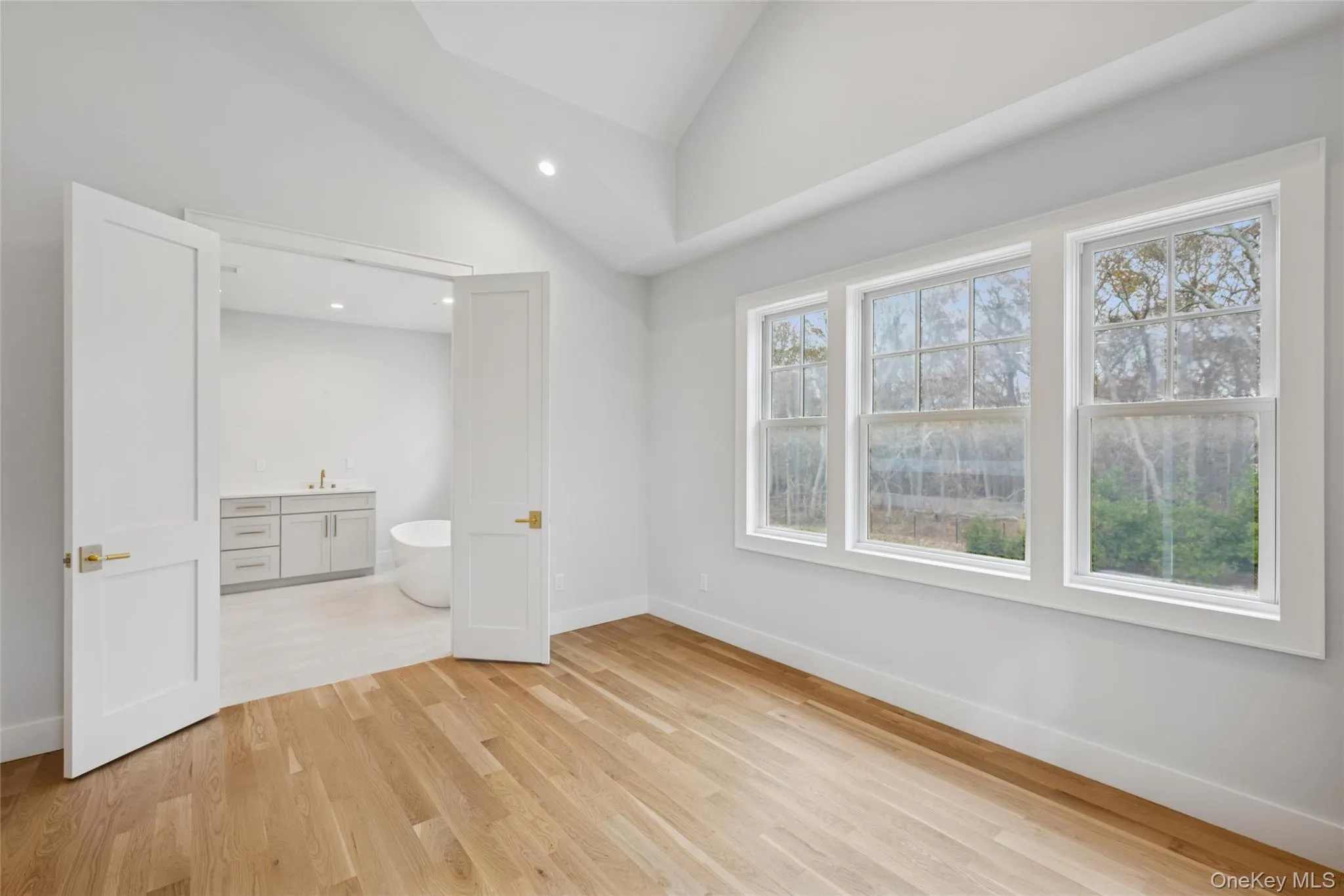 Primary bedroom featuring lofted ceiling, light wood-type flooring, ensuite bath, and recessed lighting Primary bedroom featuring lofted ceiling, light wood-type flooring, ensuite bath, and recessed lighting