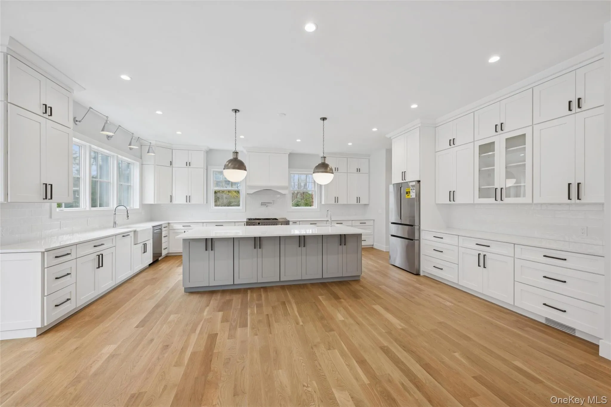 Kitchen featuring tasteful backsplash, a kitchen island with sink, glass insert cabinets, hanging light fixtures, and recessed lighting Kitchen featuring tasteful backsplash, a kitchen island with sink, glass insert cabinets, hanging light fixtures, and recessed lighting