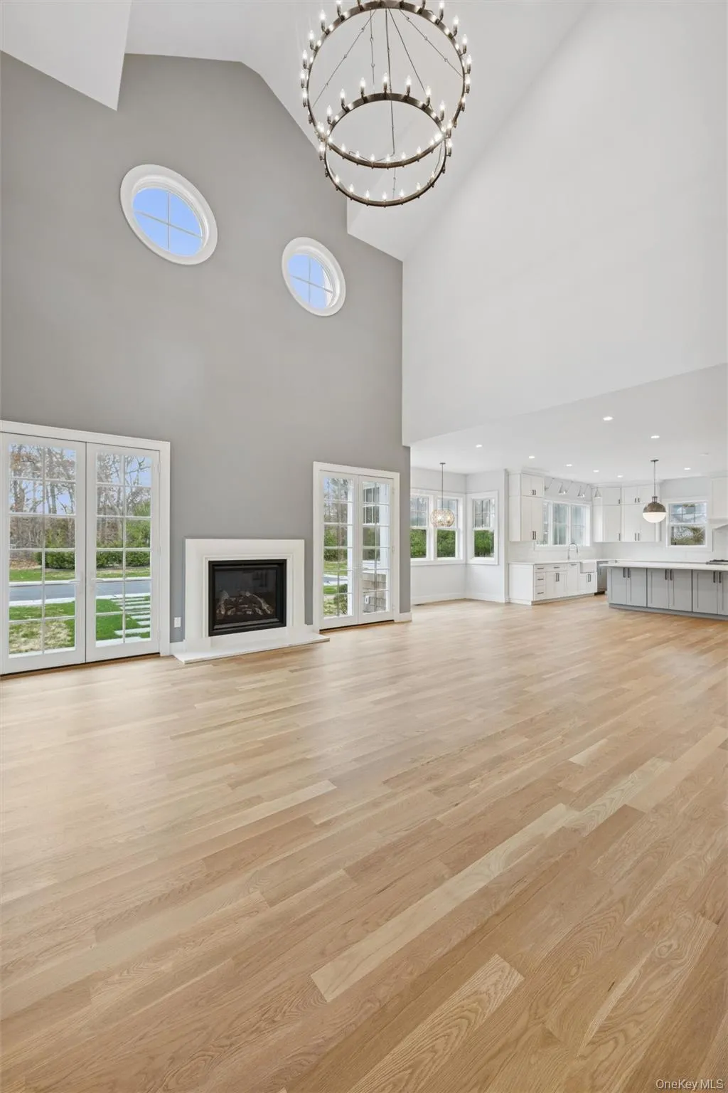 Living room featuring a glass covered fireplace, a chandelier, light wood-style floors, healthy amount of natural light, and high vaulted ceiling Living room featuring a glass covered fireplace, a chandelier, light wood-style floors, healthy amount of natural light, and high vaulted ceiling