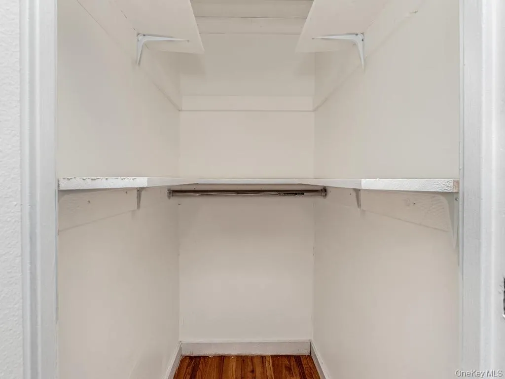 Recessed closet featuring wood-finish flooring, white painted walls, and built-in shelving with hanging rod Recessed closet featuring wood-finish flooring, white painted walls, and built-in shelving with hanging rod