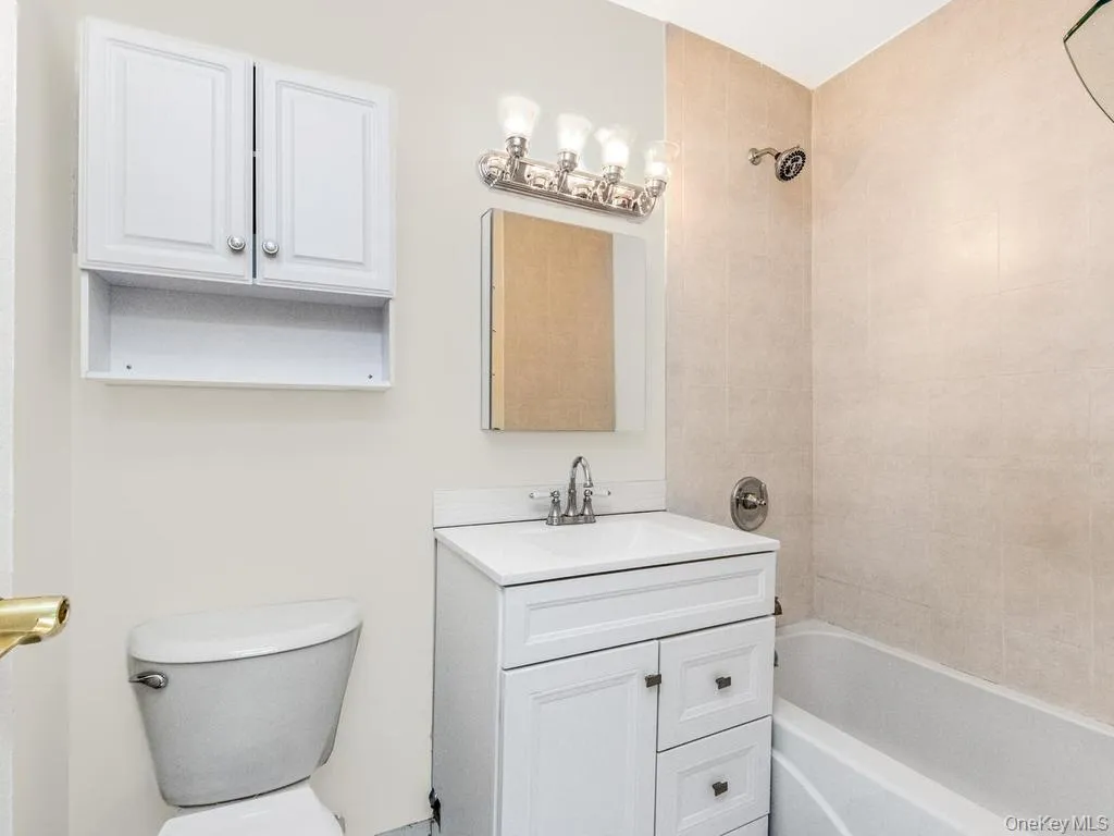 Full bathroom featuring a white vanity with integrated sink, chrome faucet, wall-mounted light fixture, and a bathtub with a shower Full bathroom featuring a white vanity with integrated sink, chrome faucet, wall-mounted light fixture, and a bathtub with a shower