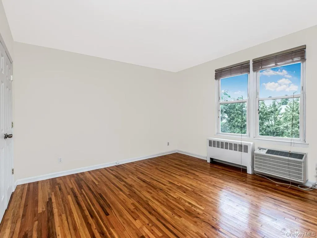 Bright room featuring wood-finish flooring, white walls, and a multi-pane window with wood-look blinds Bright room featuring wood-finish flooring, white walls, and a multi-pane window with wood-look blinds