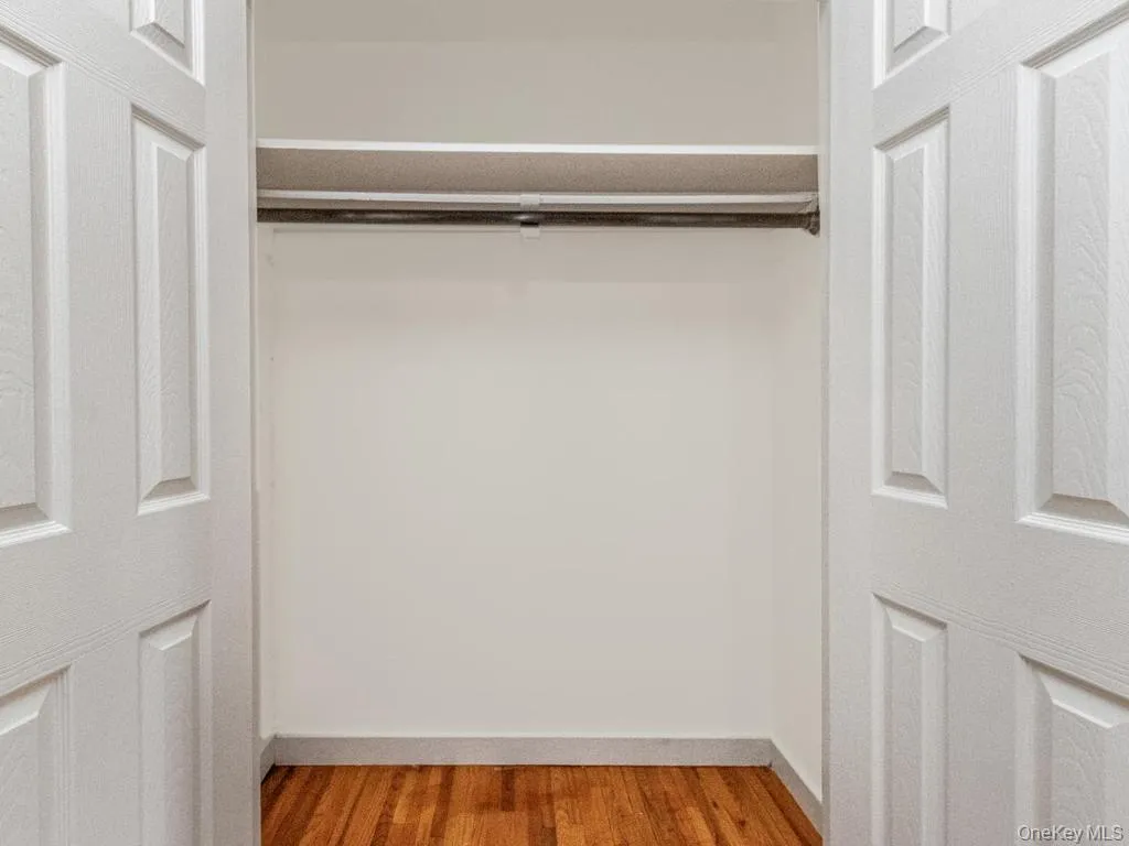Recessed closet featuring white panel doors, wood-finish flooring, a built-in hanging rod, and an upper shelf Recessed closet featuring white panel doors, wood-finish flooring, a built-in hanging rod, and an upper shelf