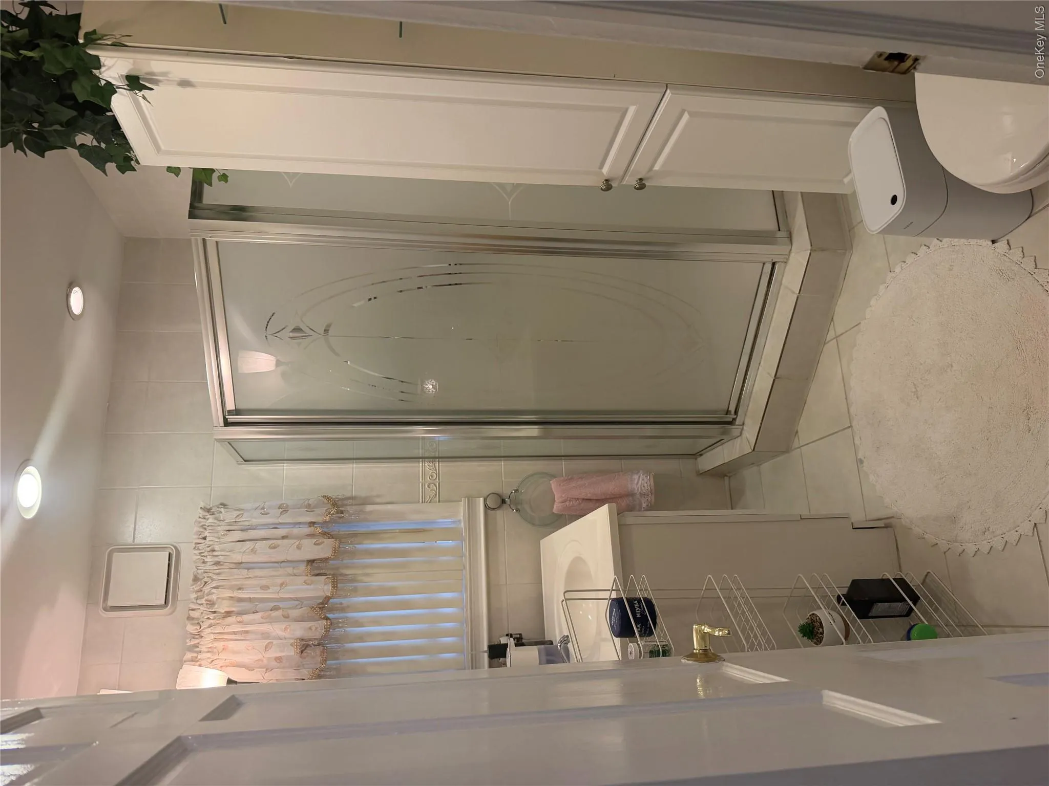 Tiled bathroom featuring a corner shower with frosted glass doors, white vanity with integrated sink, and recessed lighting Tiled bathroom featuring a corner shower with frosted glass doors, white vanity with integrated sink, and recessed lighting