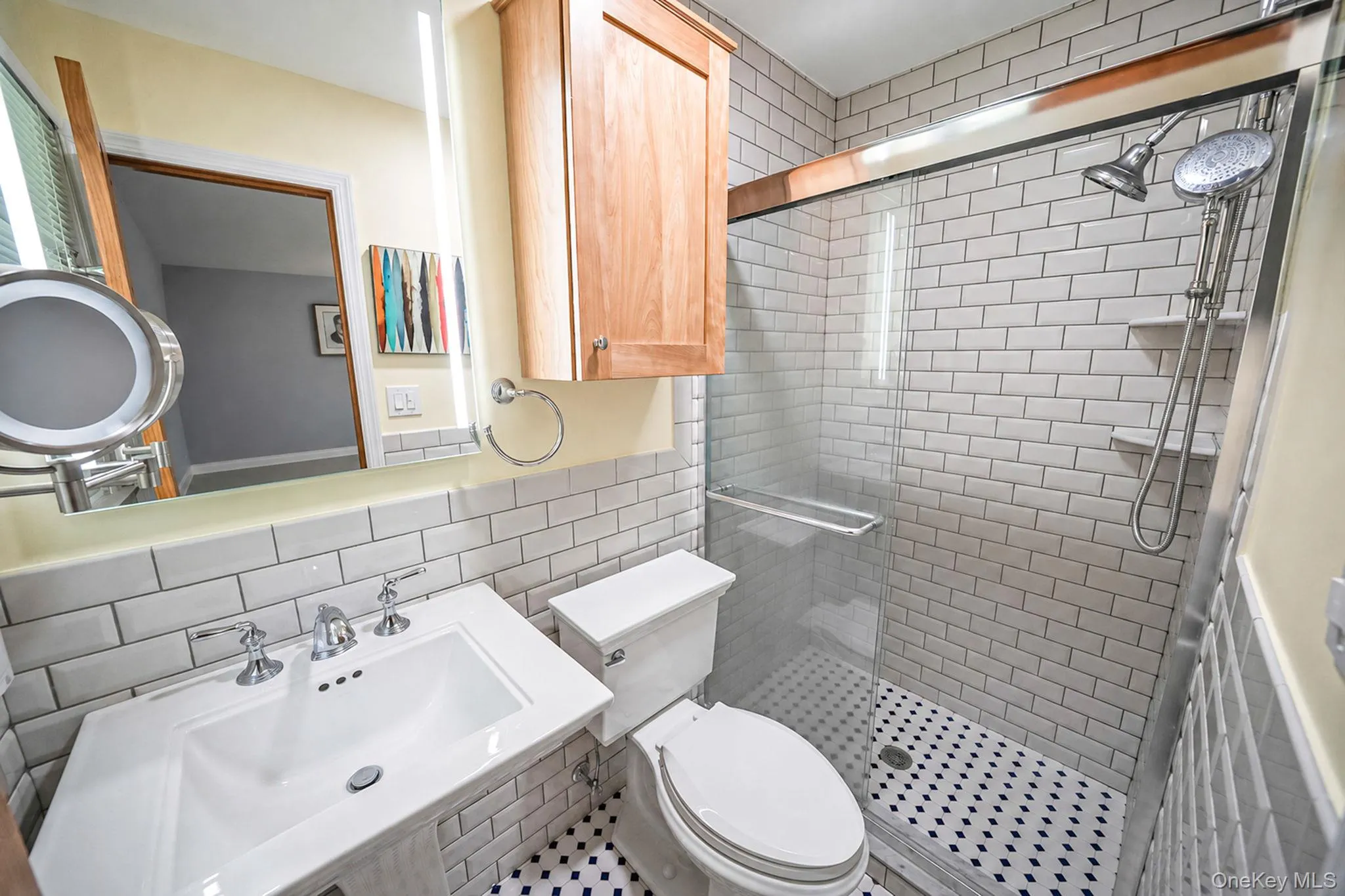 White subway tile half-wall, single vanity with chrome faucet, built-in wooden cabinet, glass-enclosed shower with subway tile surround, and black and white patterned floor tile White subway tile half-wall, single vanity with chrome faucet, built-in wooden cabinet, glass-enclosed shower with subway tile surround, and black and white patterned floor tile