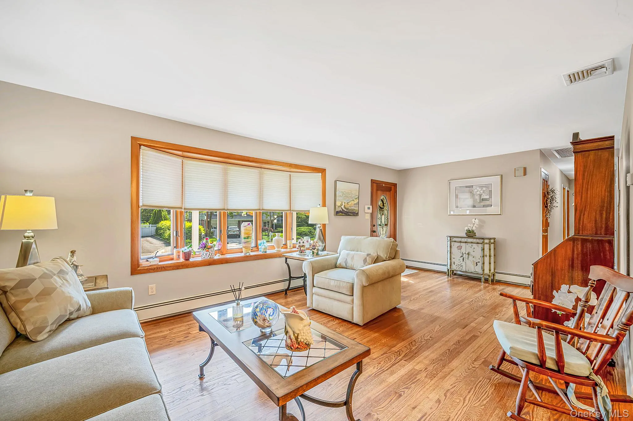 Hardwood flooring, bay window with wood trim, wood-paneled staircase, and neutral wall tones Hardwood flooring, bay window with wood trim, wood-paneled staircase, and neutral wall tones