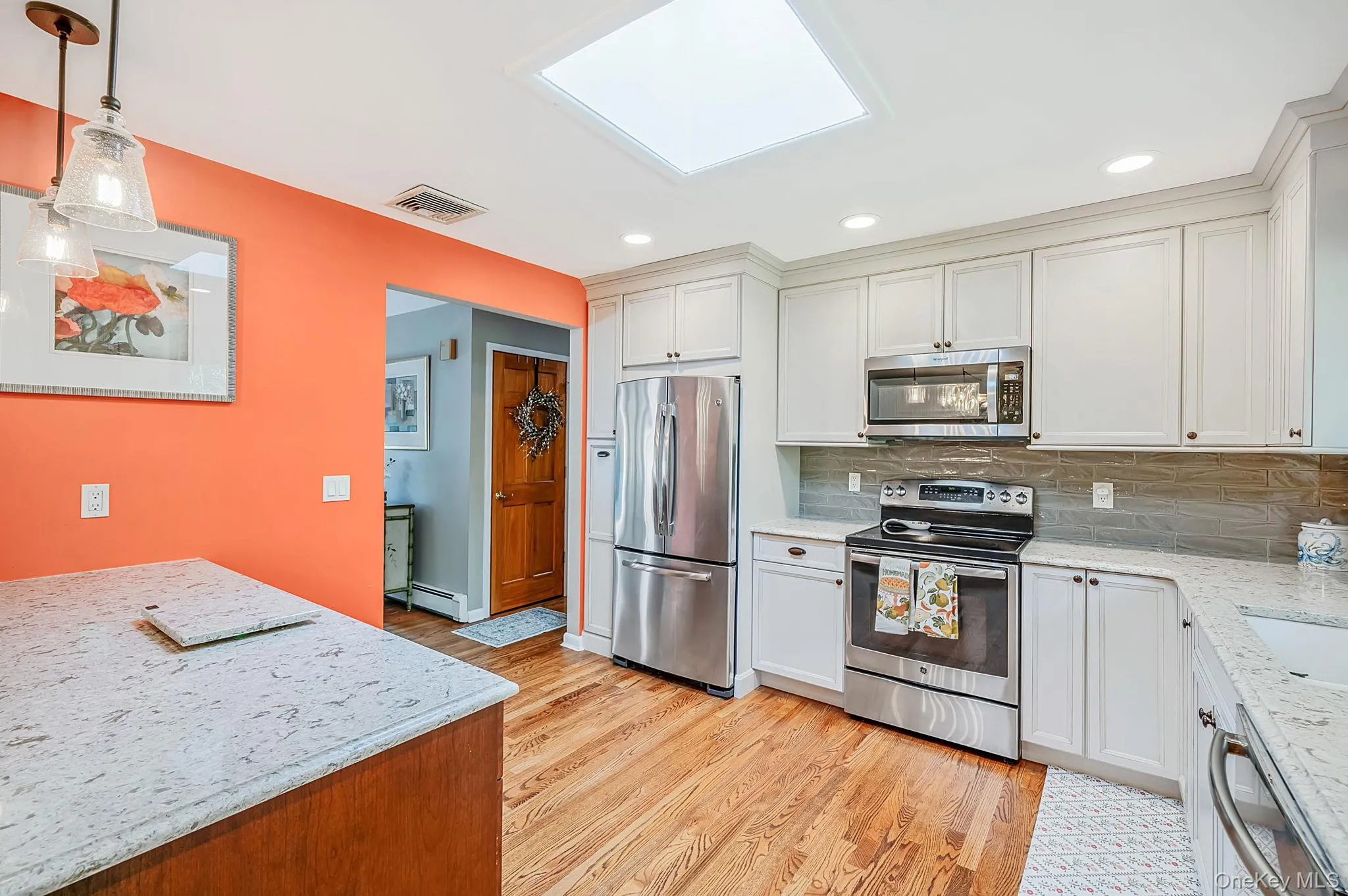 Sky-lit kitchen featuring wood-finish flooring, white cabinetry, stainless steel appliances, and light-toned countertops Sky-lit kitchen featuring wood-finish flooring, white cabinetry, stainless steel appliances, and light-toned countertops
