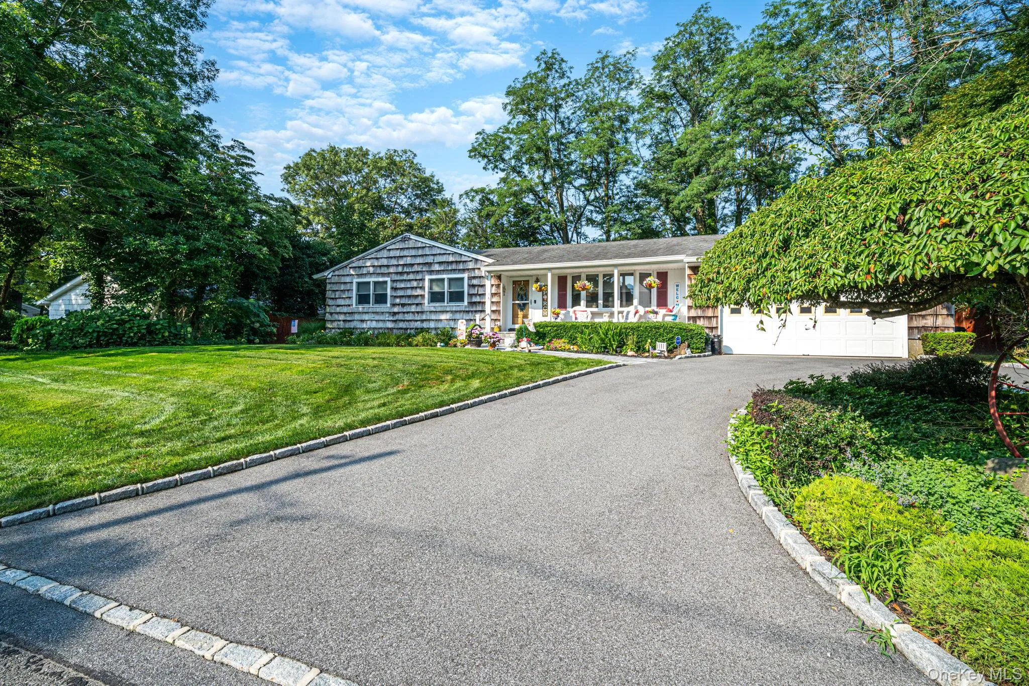 Charming ranch-style residence featuring a curved asphalt driveway with concrete edging, manicured lawn, and mature landscaping including established shade trees and ivy-covered perimeter plantings Charming ranch-style residence featuring a curved asphalt driveway with concrete edging, manicured lawn, and mature landscaping including established shade trees and ivy-covered perimeter plantings