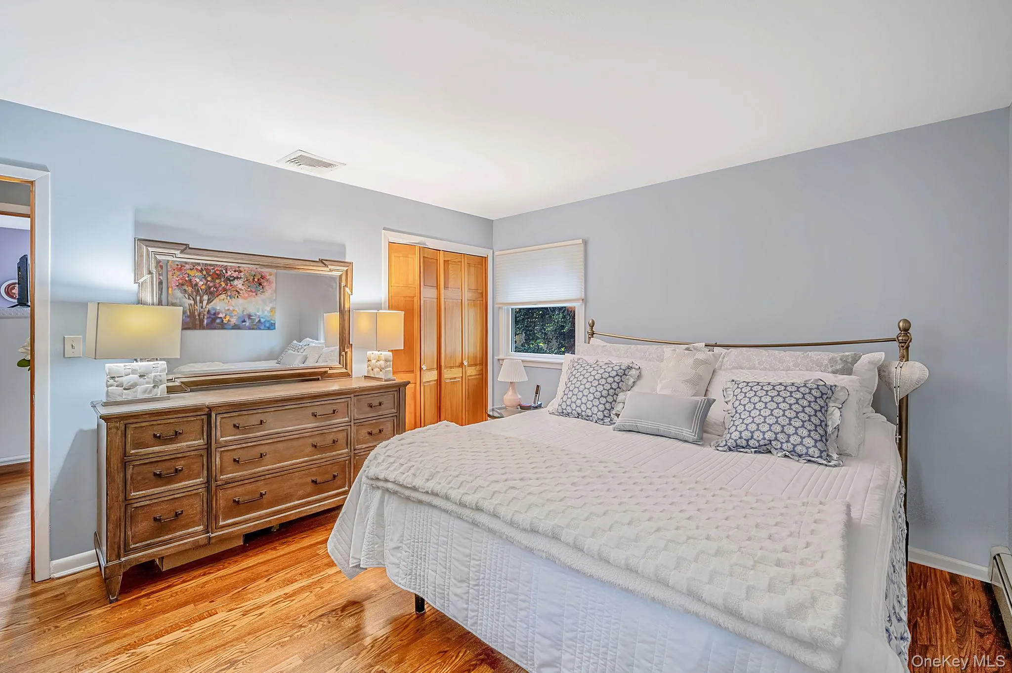Hardwood flooring, light blue wall paint, window with roller shade, and warm-toned wood bi-fold closet doors Hardwood flooring, light blue wall paint, window with roller shade, and warm-toned wood bi-fold closet doors