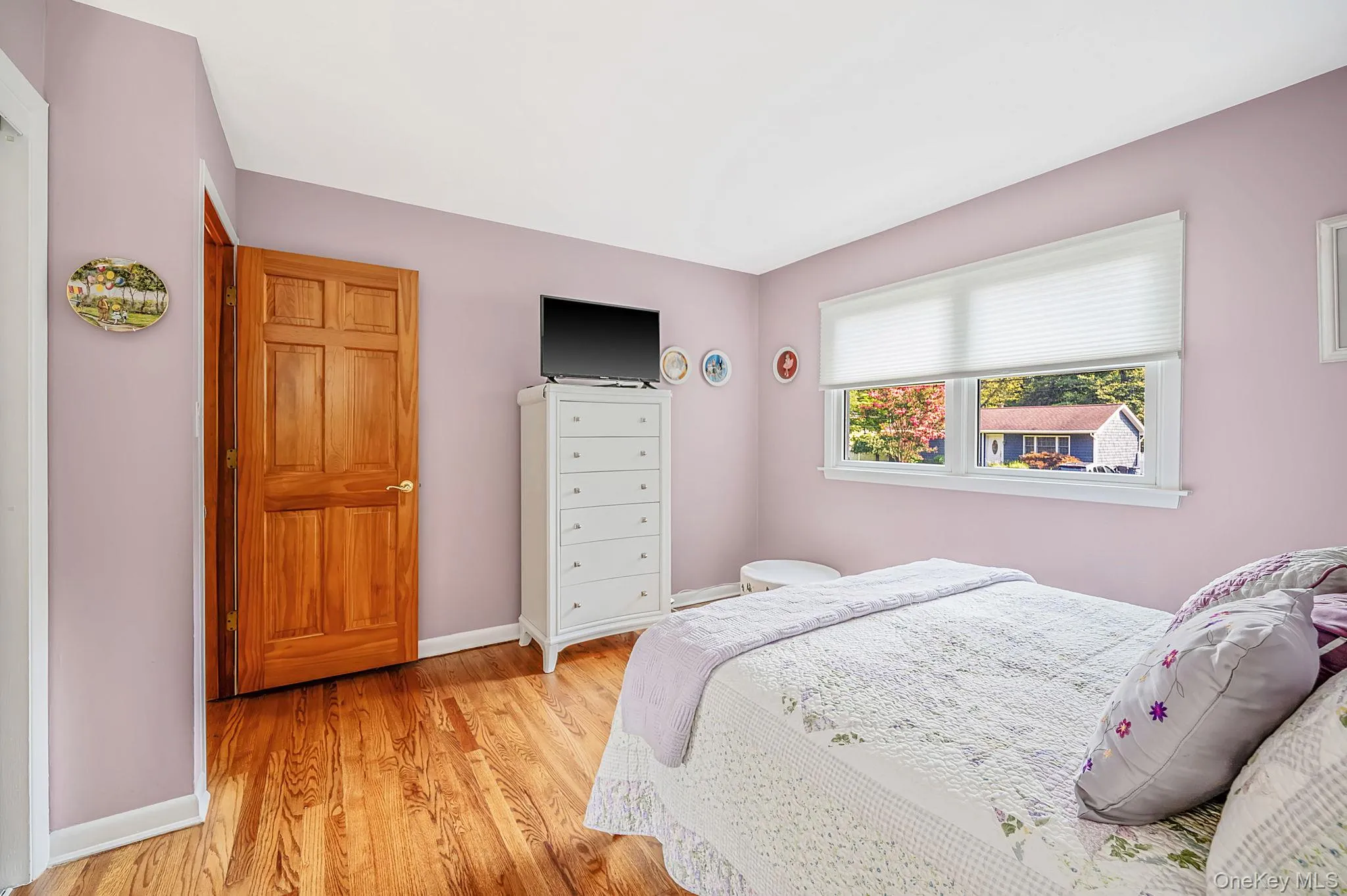 Hardwood flooring, natural wood panel door, white trim, window with cellular shades, and neutral wall color Hardwood flooring, natural wood panel door, white trim, window with cellular shades, and neutral wall color