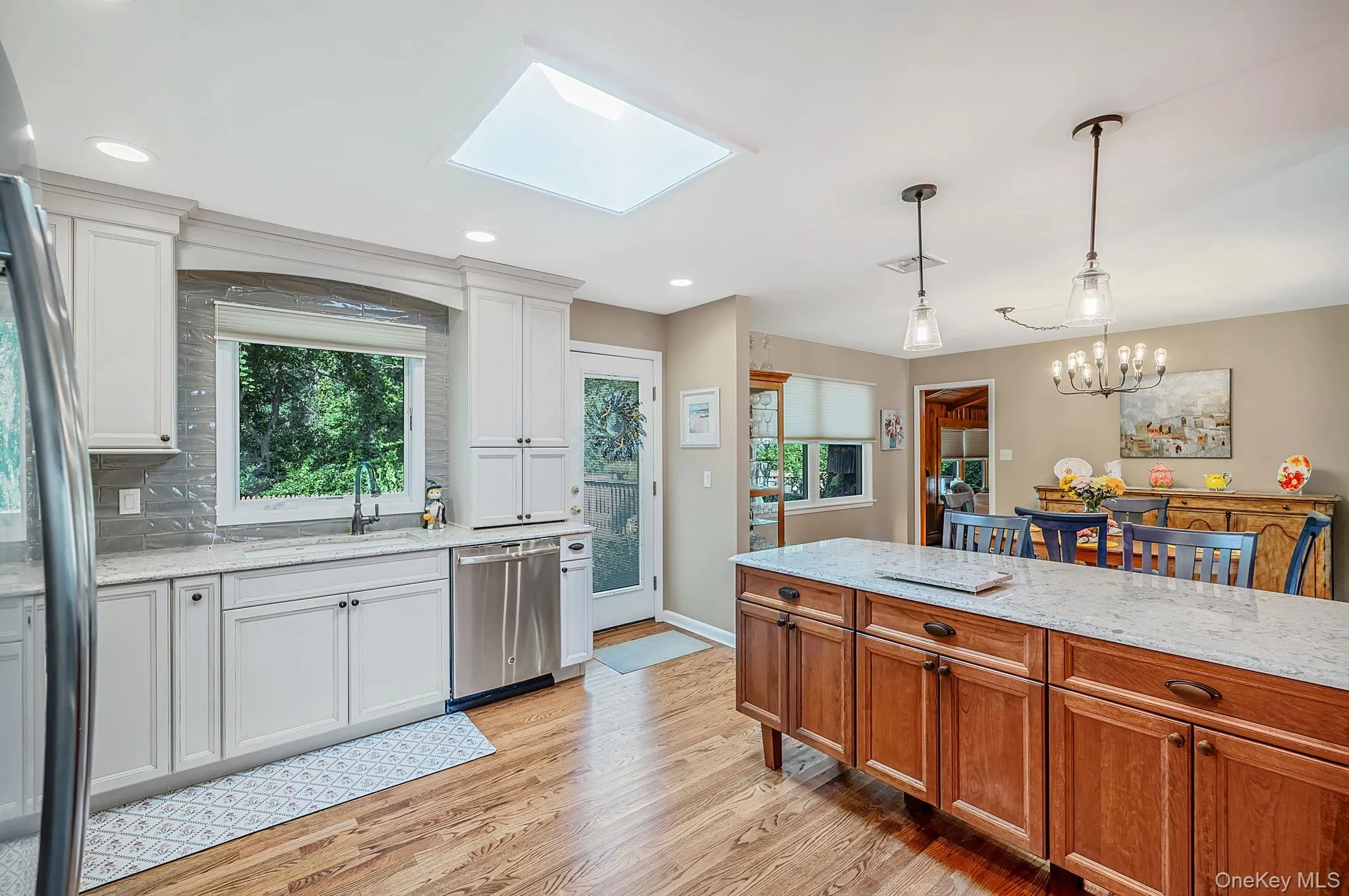 Kitchen featuring white cabinetry, wood-finish flooring, a central island with a light-toned countertop, stainless steel appliances, and a skylight Kitchen featuring white cabinetry, wood-finish flooring, a central island with a light-toned countertop, stainless steel appliances, and a skylight