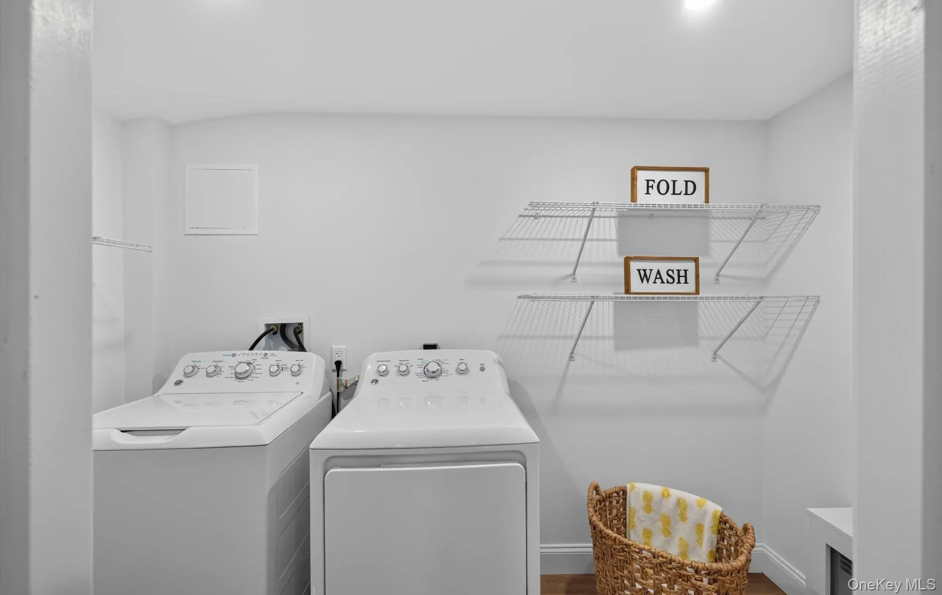 Dedicated laundry area featuring white walls, overhead wire shelving, and wood-finish flooring Dedicated laundry area featuring white walls, overhead wire shelving, and wood-finish flooring