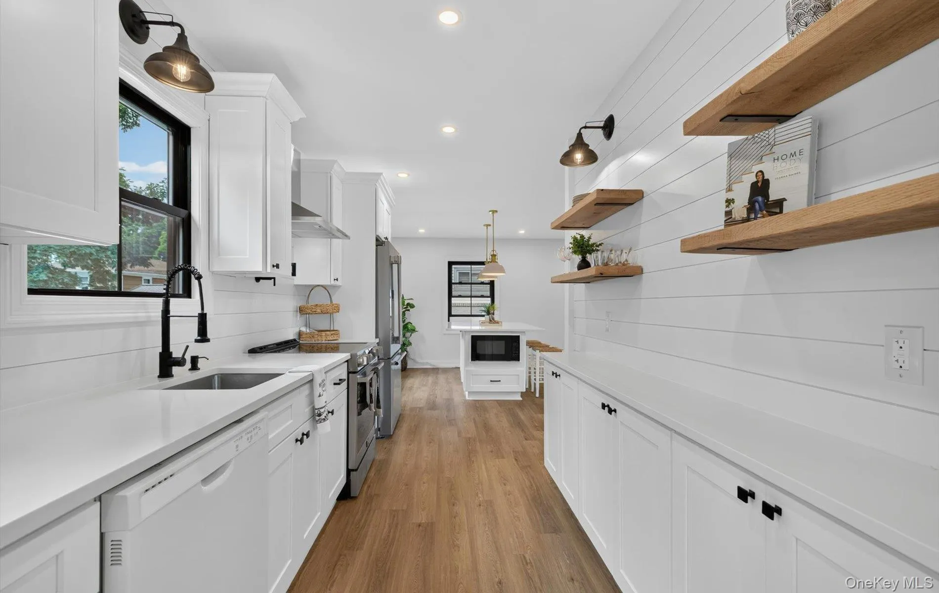 Modern kitchen featuring white shaker cabinetry, light wood-finish flooring, white countertops, black matte fixtures, and open wood shelving Modern kitchen featuring white shaker cabinetry, light wood-finish flooring, white countertops, black matte fixtures, and open wood shelving