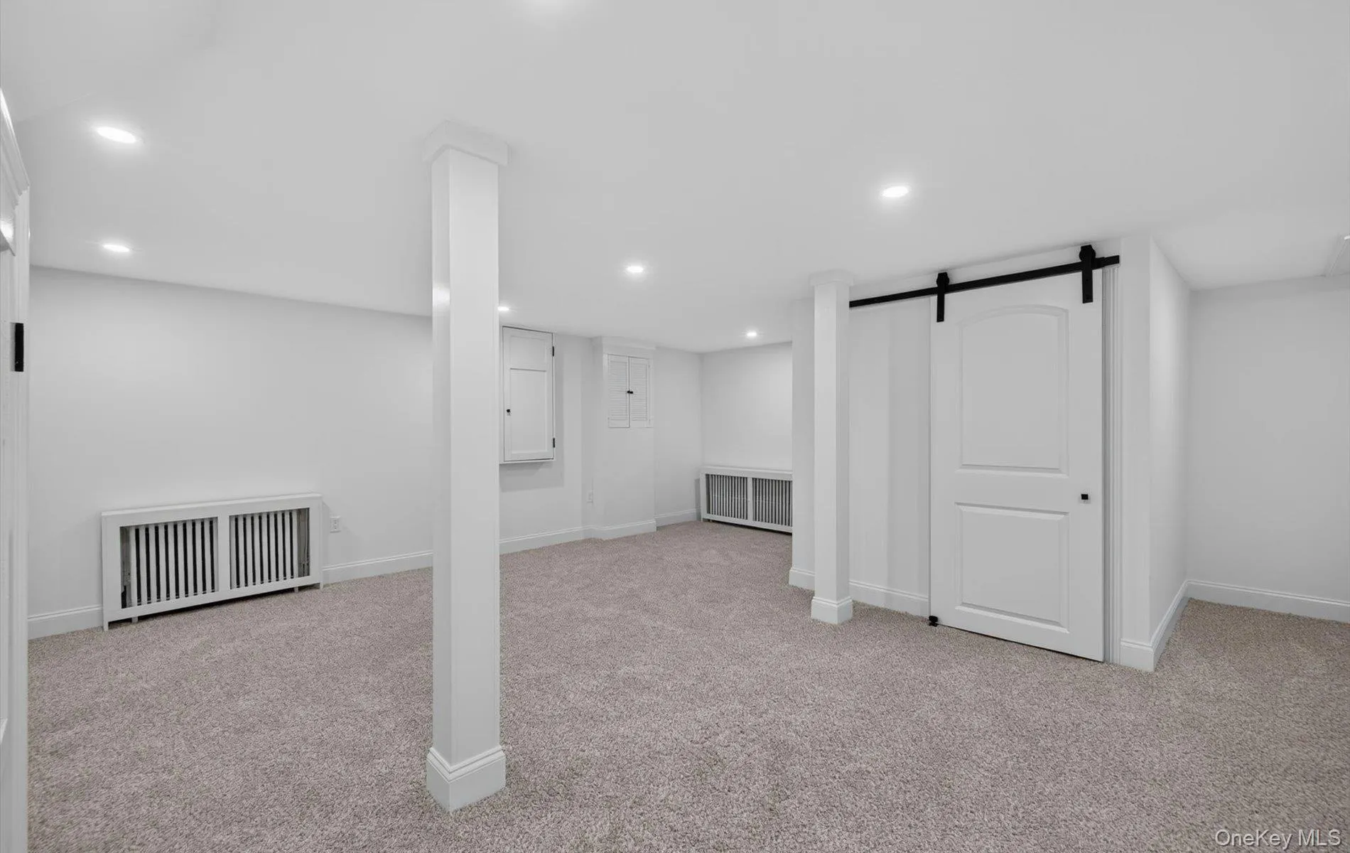 Spacious room featuring light gray carpeting, recessed ceiling lighting, a white barn door with black hardware, and white trim Spacious room featuring light gray carpeting, recessed ceiling lighting, a white barn door with black hardware, and white trim