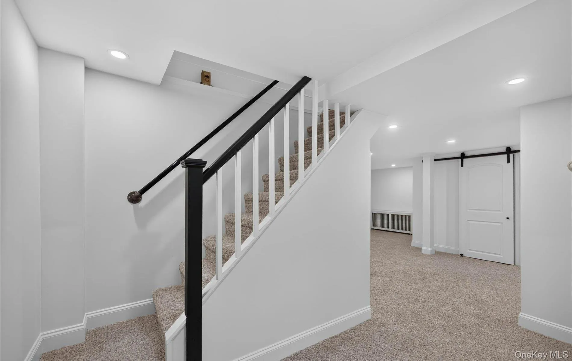 Carpeted staircase with black newel post and handrail, white balusters, and recessed lighting Carpeted staircase with black newel post and handrail, white balusters, and recessed lighting