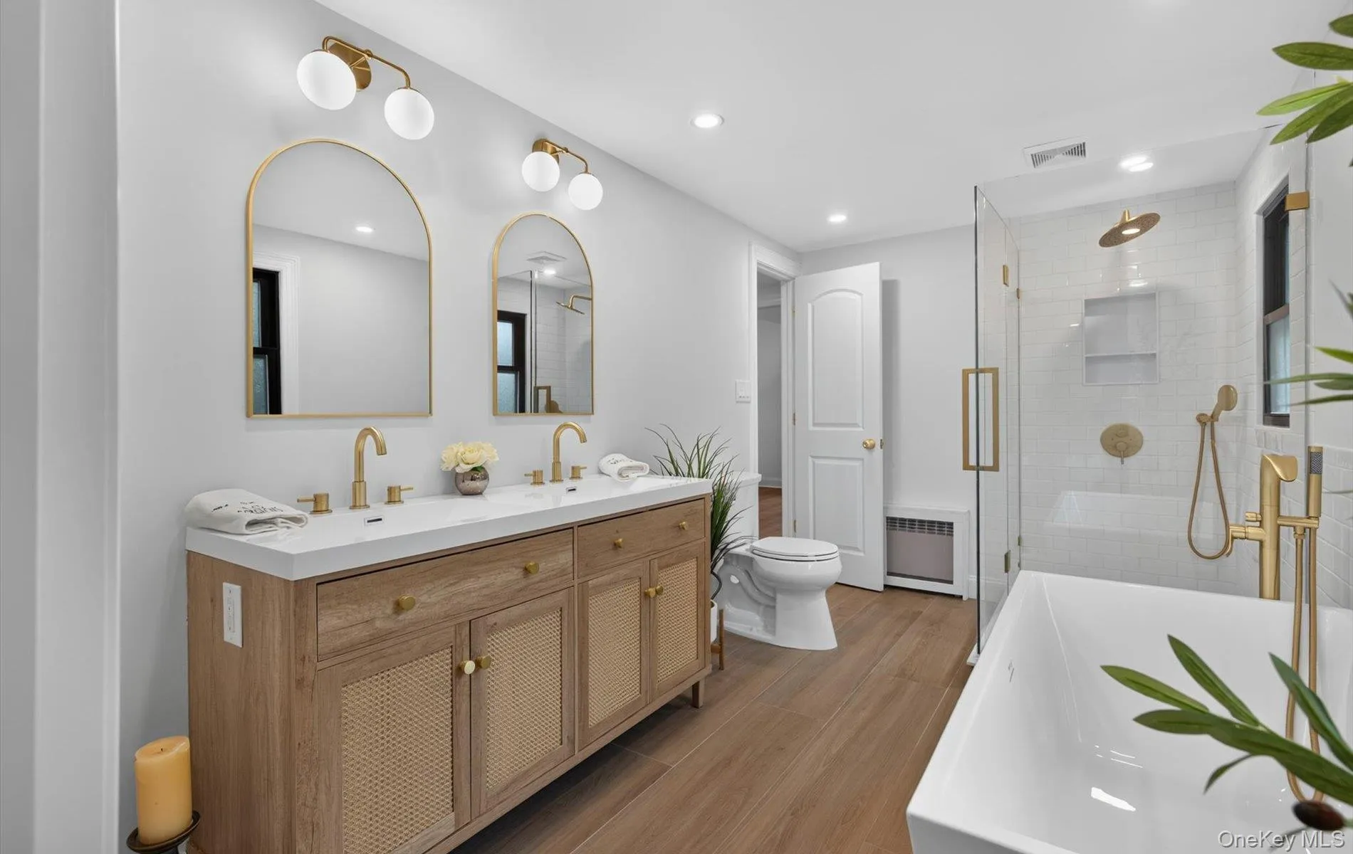 Contemporary bathroom featuring a double vanity with wood-finish cabinetry, arched mirrors, and a white countertop with integrated sinks Contemporary bathroom featuring a double vanity with wood-finish cabinetry, arched mirrors, and a white countertop with integrated sinks