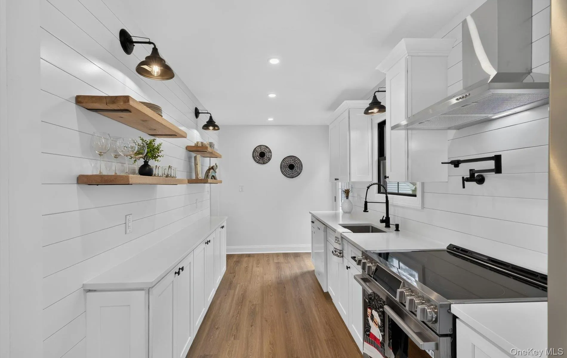 Galley-style kitchen featuring shiplap walls, white cabinetry, wood-finish flooring, recessed lighting, and a stainless steel range hood Galley-style kitchen featuring shiplap walls, white cabinetry, wood-finish flooring, recessed lighting, and a stainless steel range hood