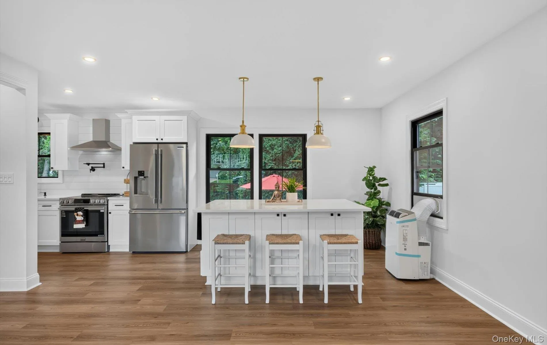 Open-concept kitchen with a central island featuring pendant lighting, white cabinetry, stainless steel appliances, and wood-finish flooring Open-concept kitchen with a central island featuring pendant lighting, white cabinetry, stainless steel appliances, and wood-finish flooring