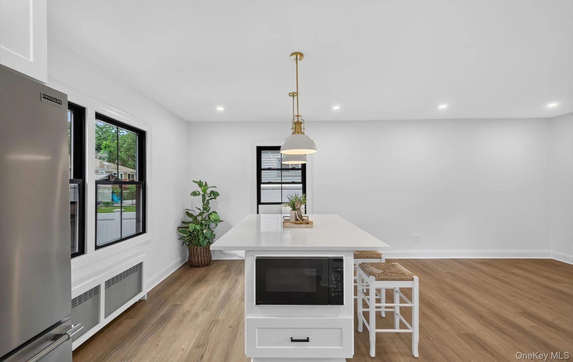 Bright, open-concept kitchen and dining area featuring a central island with integrated microwave, recessed lighting, and wood-finish flooring Bright, open-concept kitchen and dining area featuring a central island with integrated microwave, recessed lighting, and wood-finish flooring