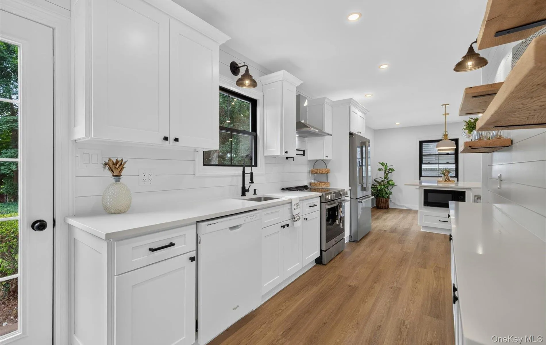 Modern kitchen featuring white shaker cabinetry, quartz countertops, stainless steel appliances, wood-finish flooring, and open shelving with industrial lighting Modern kitchen featuring white shaker cabinetry, quartz countertops, stainless steel appliances, wood-finish flooring, and open shelving with industrial lighting