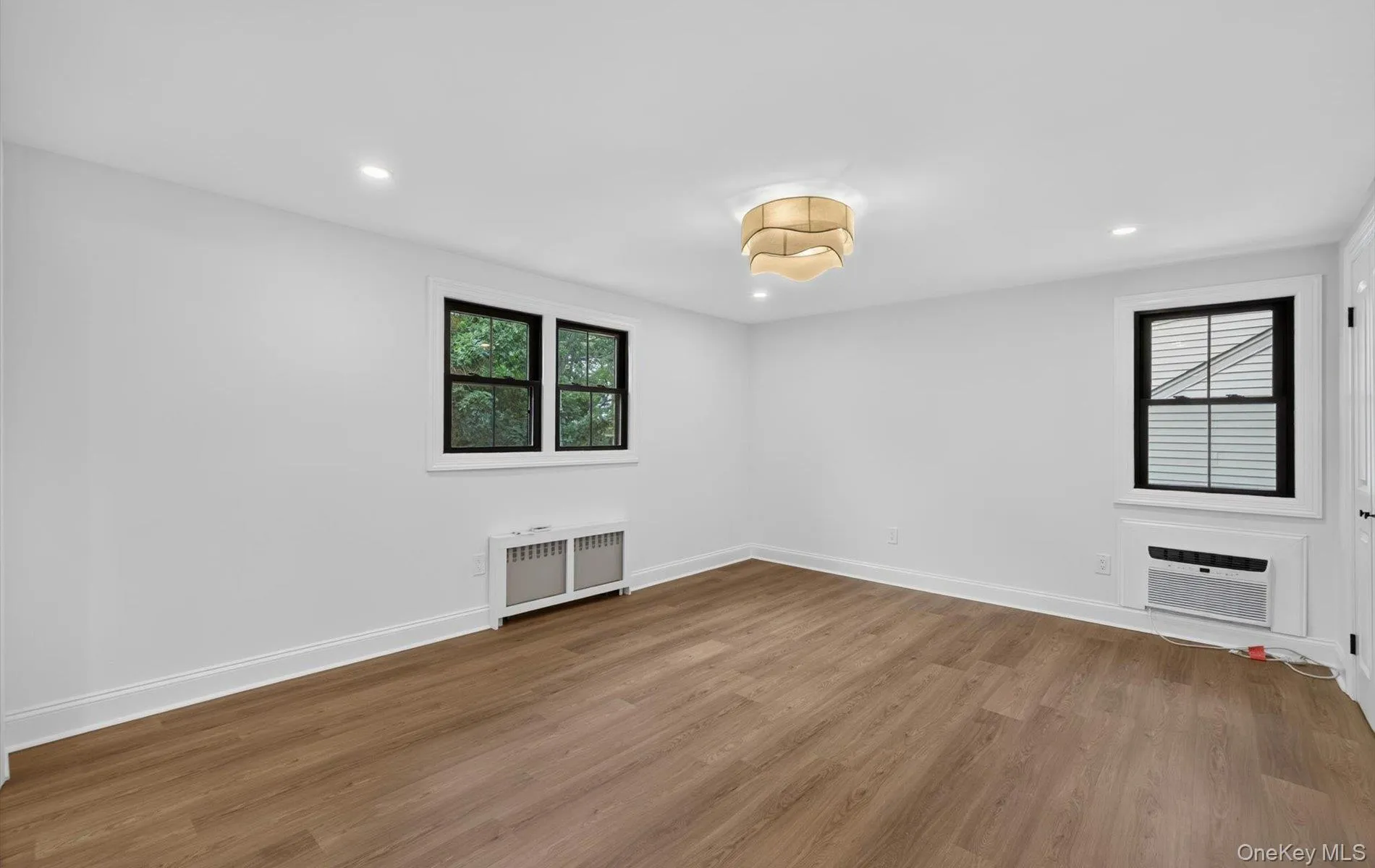 Bright room featuring wood-finish flooring, recessed lighting, and a contemporary ceiling fixture Bright room featuring wood-finish flooring, recessed lighting, and a contemporary ceiling fixture