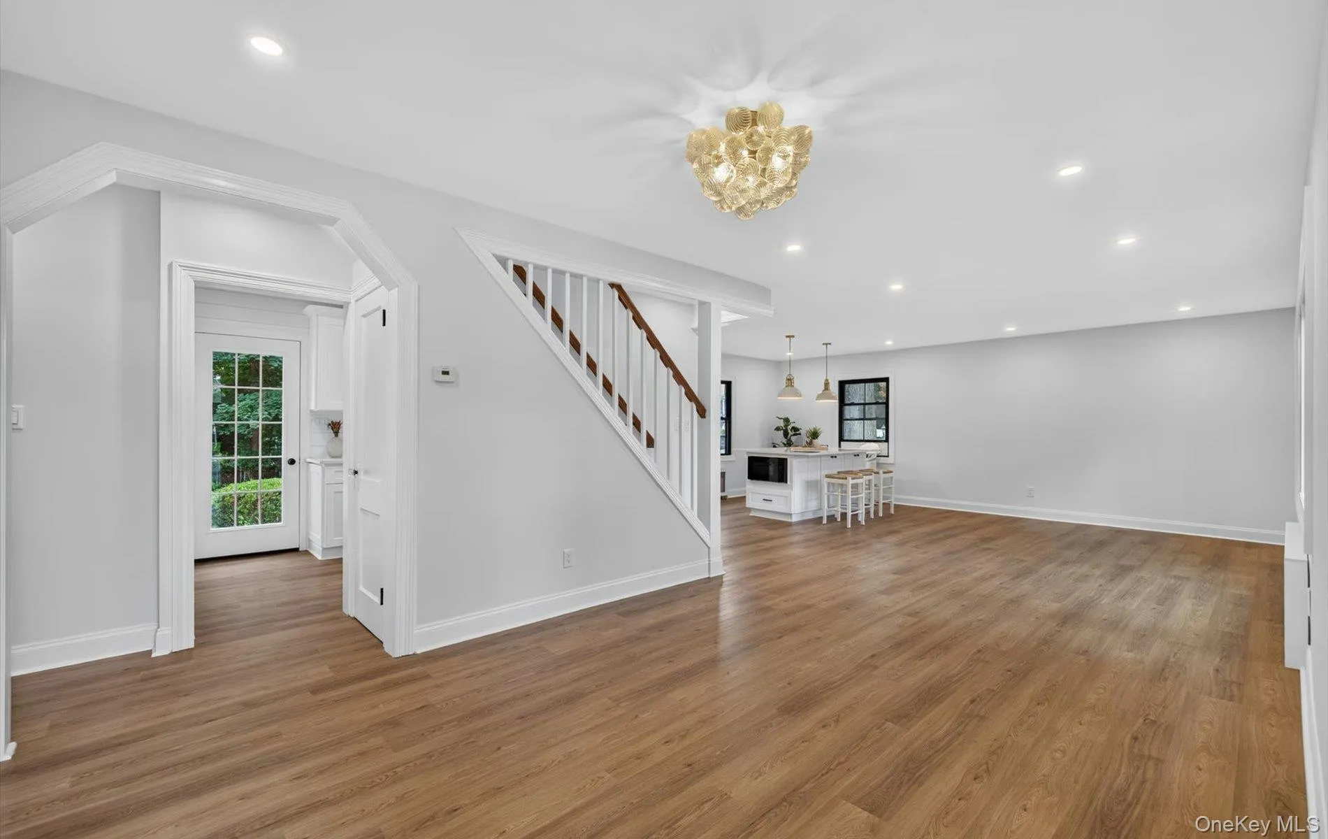Spacious open-concept living area featuring wood-finish flooring, recessed lighting, and a decorative ceiling fixture Spacious open-concept living area featuring wood-finish flooring, recessed lighting, and a decorative ceiling fixture