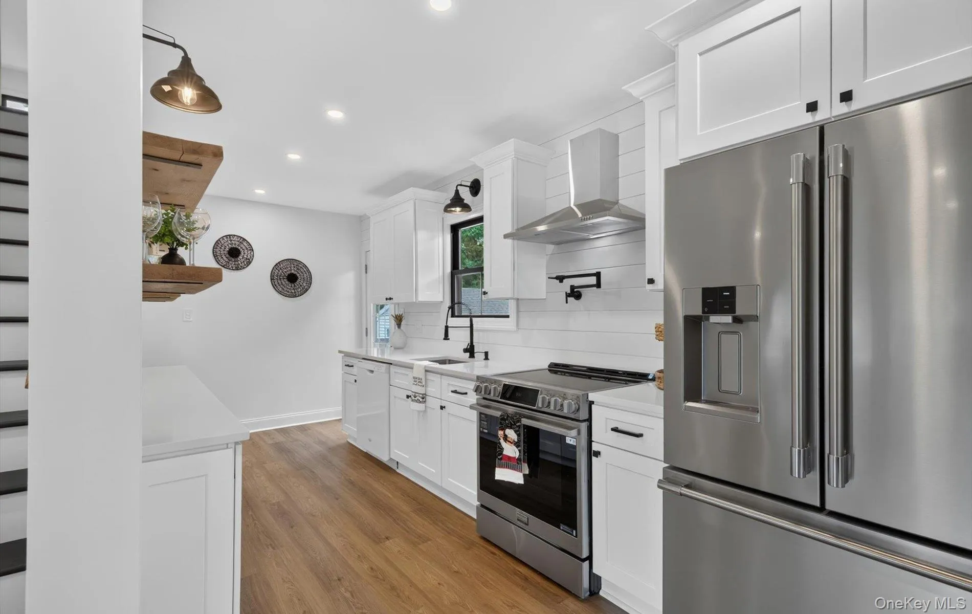 Modern kitchen featuring white shaker cabinetry, stainless steel appliances, wood-finish flooring, recessed lighting, and a pot filler faucet Modern kitchen featuring white shaker cabinetry, stainless steel appliances, wood-finish flooring, recessed lighting, and a pot filler faucet