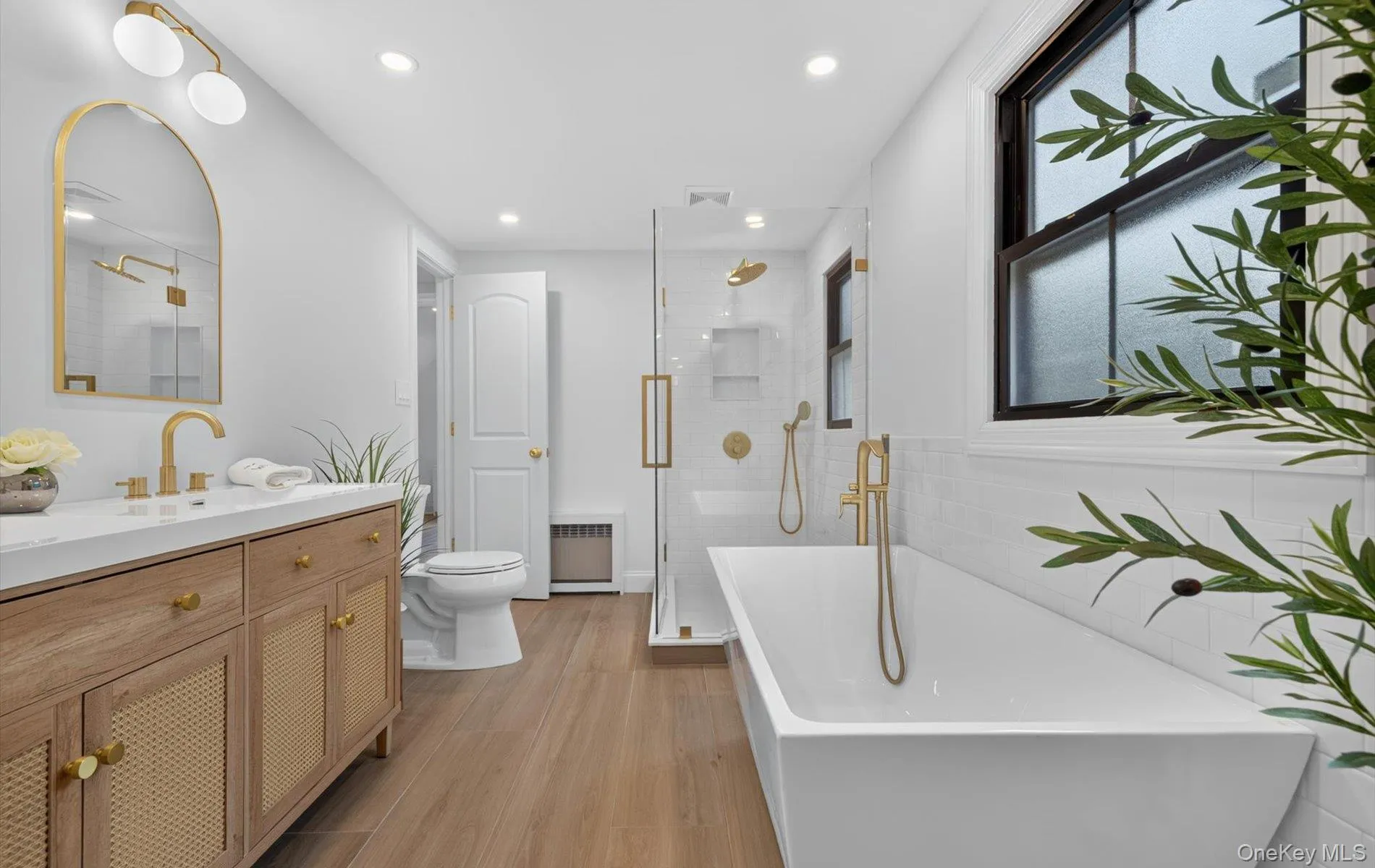 Freestanding soaking tub with floor-mounted faucet, wood-finish flooring, and white subway tile surround Freestanding soaking tub with floor-mounted faucet, wood-finish flooring, and white subway tile surround