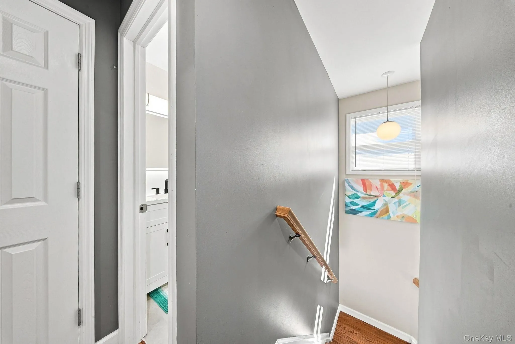 Upper-level hallway with gray walls, white trim, and a wood-finish handrail Upper-level hallway with gray walls, white trim, and a wood-finish handrail