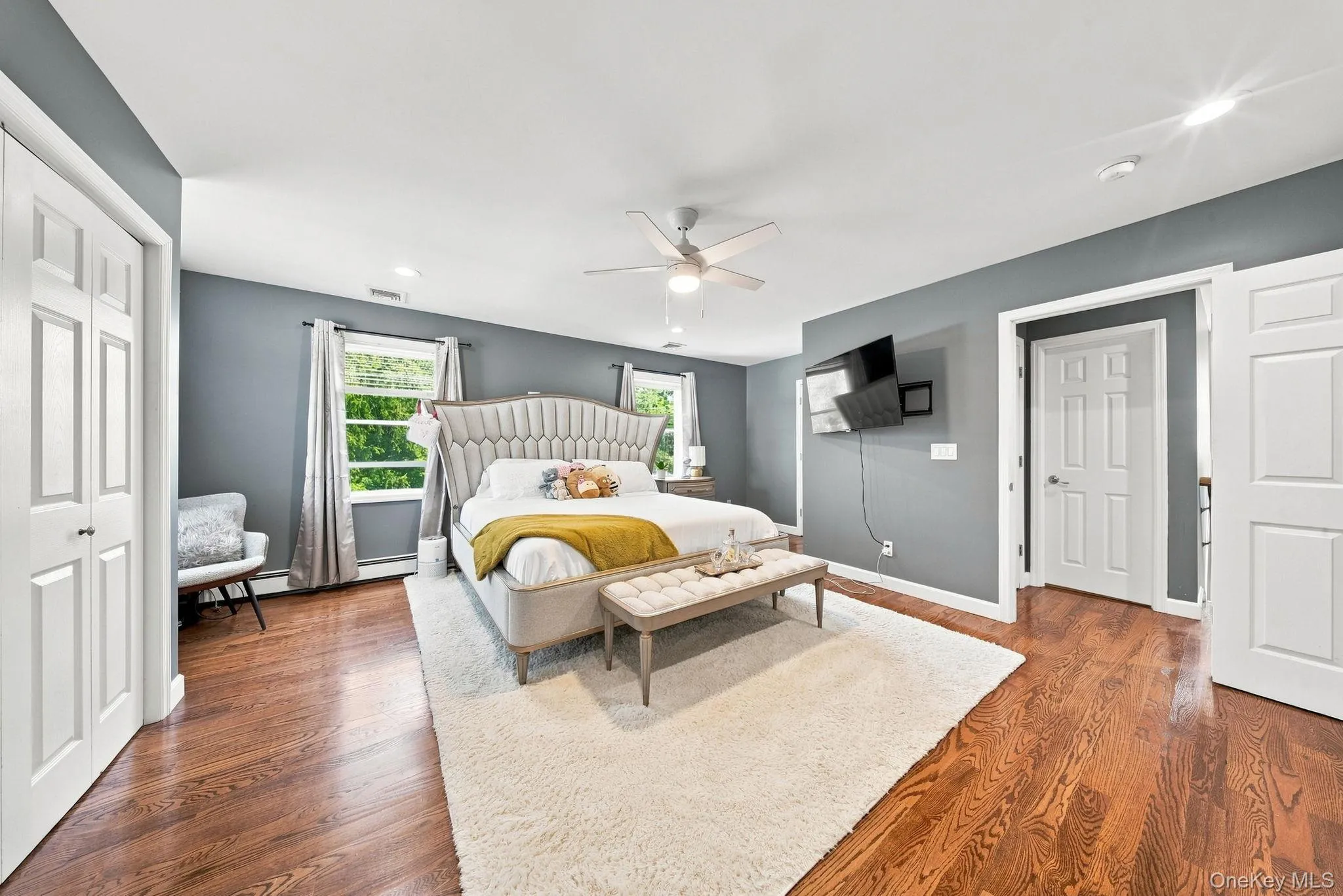 Hardwood flooring, painted walls, two windows, two paneled closet doors, and a ceiling fan with integrated lighting Hardwood flooring, painted walls, two windows, two paneled closet doors, and a ceiling fan with integrated lighting