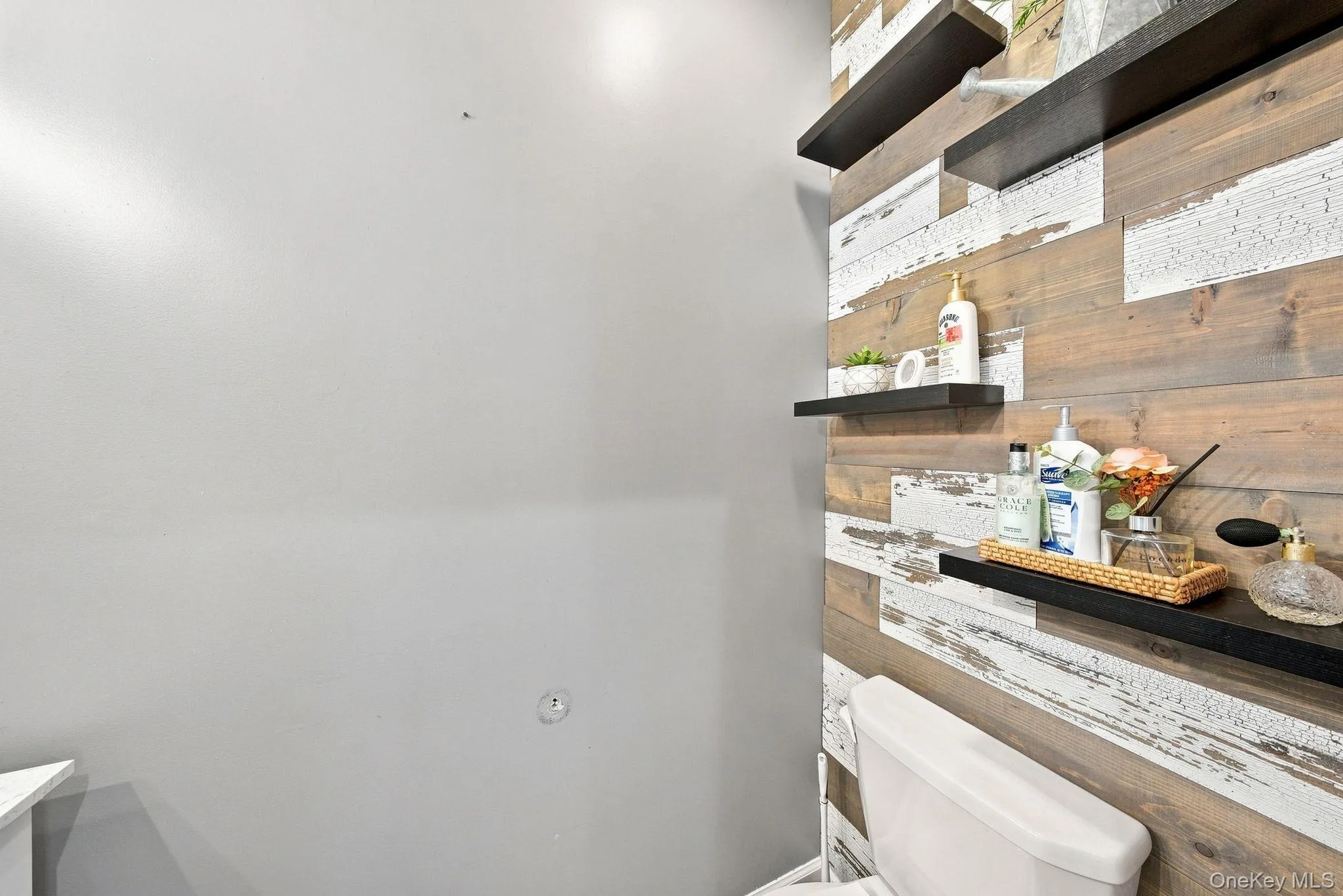 Modern half bathroom featuring stacked floating shelves with black metal frames and wood-finish backing, white subway tile walls, and a white toilet Modern half bathroom featuring stacked floating shelves with black metal frames and wood-finish backing, white subway tile walls, and a white toilet