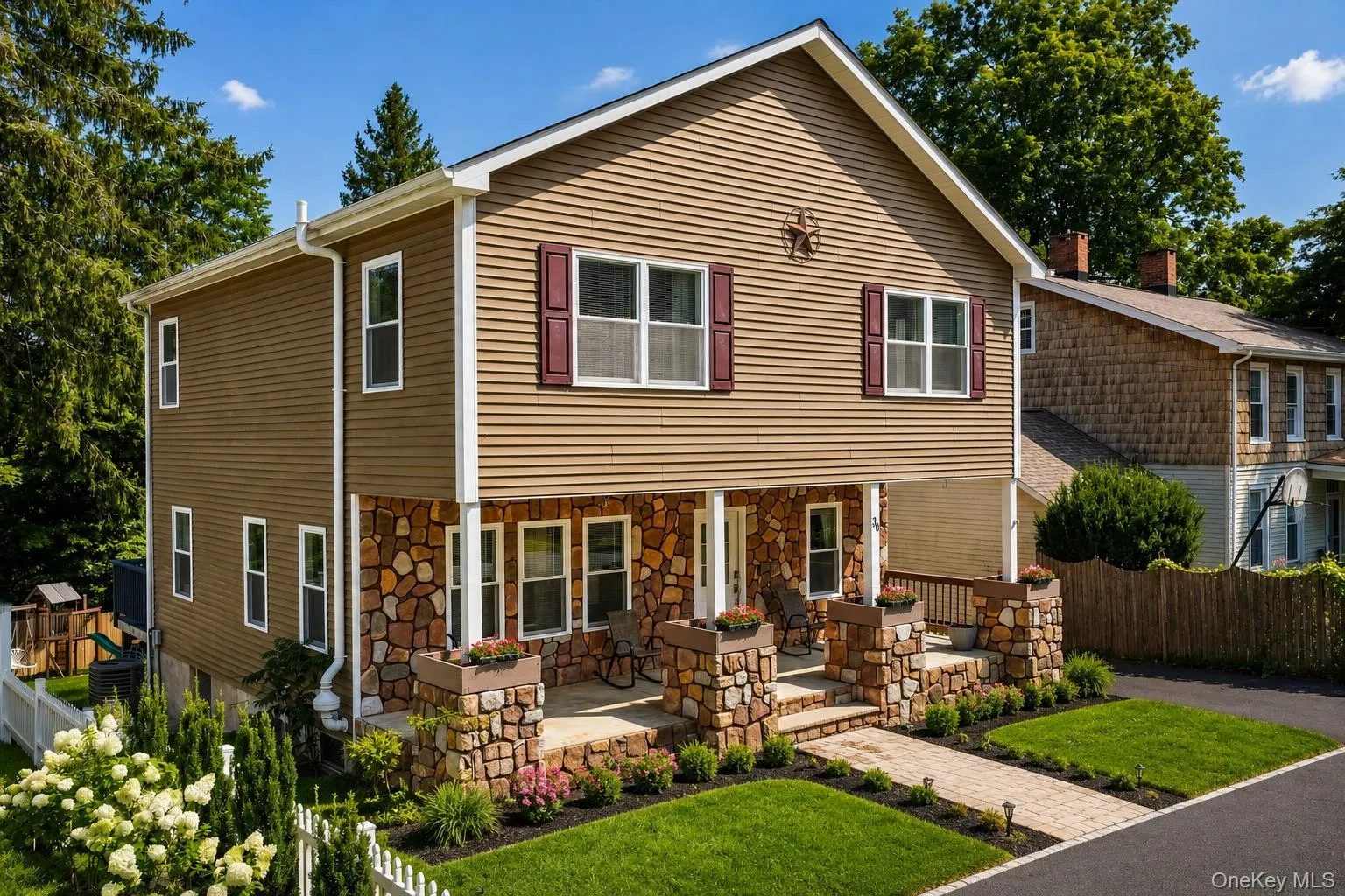 Two-story residence featuring a stone-clad porch and columns, a paver walkway, and a landscaped front yard with a white picket fence Two-story residence featuring a stone-clad porch and columns, a paver walkway, and a landscaped front yard with a white picket fence