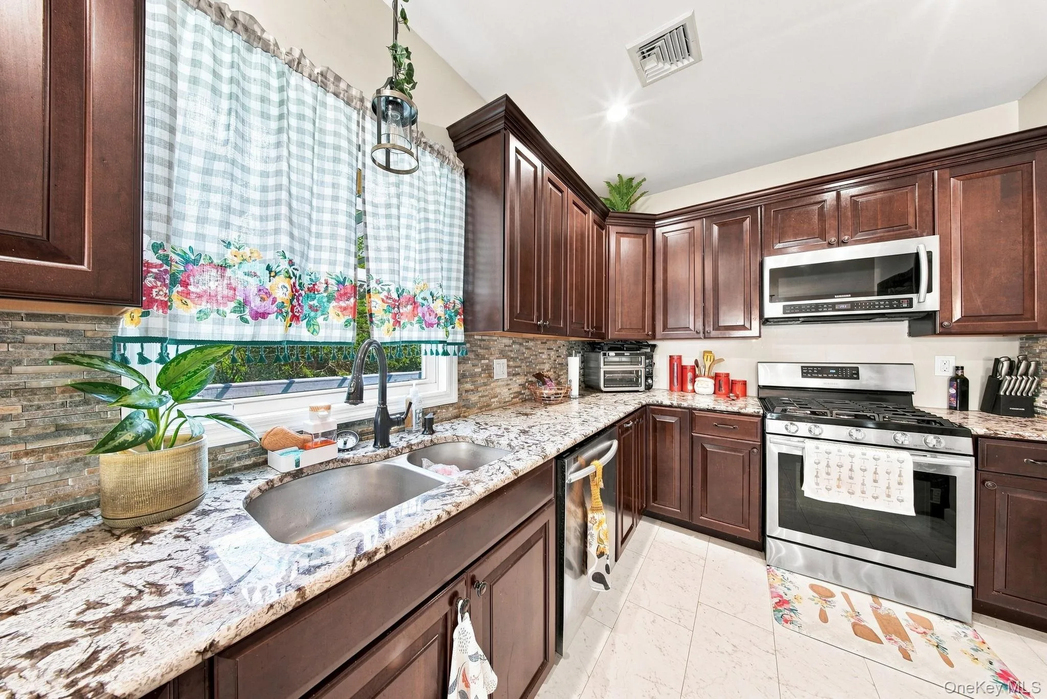 Chef's kitchen featuring rich wood cabinetry, granite countertops with waterfall edge, stainless steel appliances including double wall ovens, and a large undermount sink with gooseneck faucet Chef's kitchen featuring rich wood cabinetry, granite countertops with waterfall edge, stainless steel appliances including double wall ovens, and a large undermount sink with gooseneck faucet