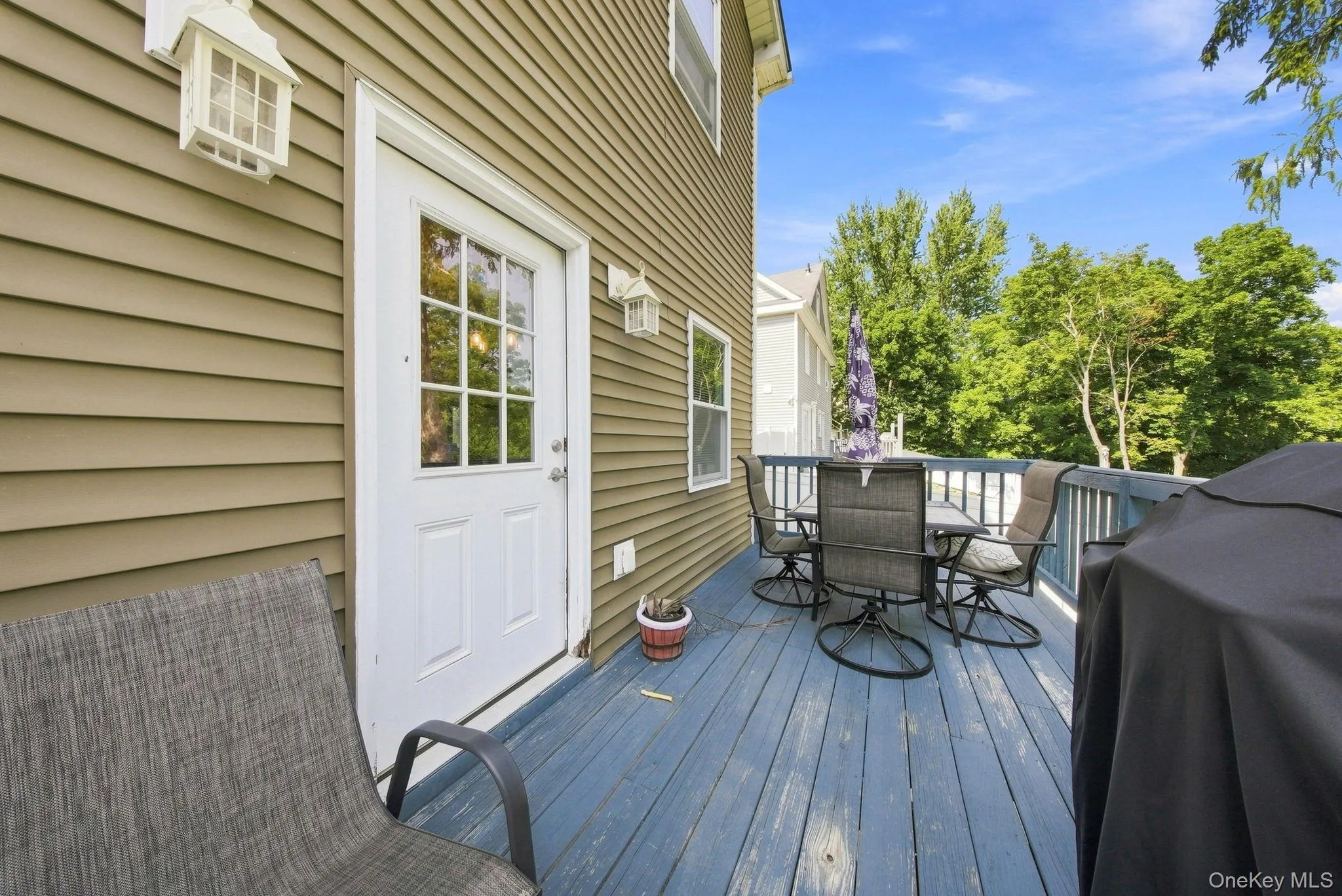 Expansive wood-finish deck with painted railings, direct outdoor access, and exterior wall lanterns Expansive wood-finish deck with painted railings, direct outdoor access, and exterior wall lanterns