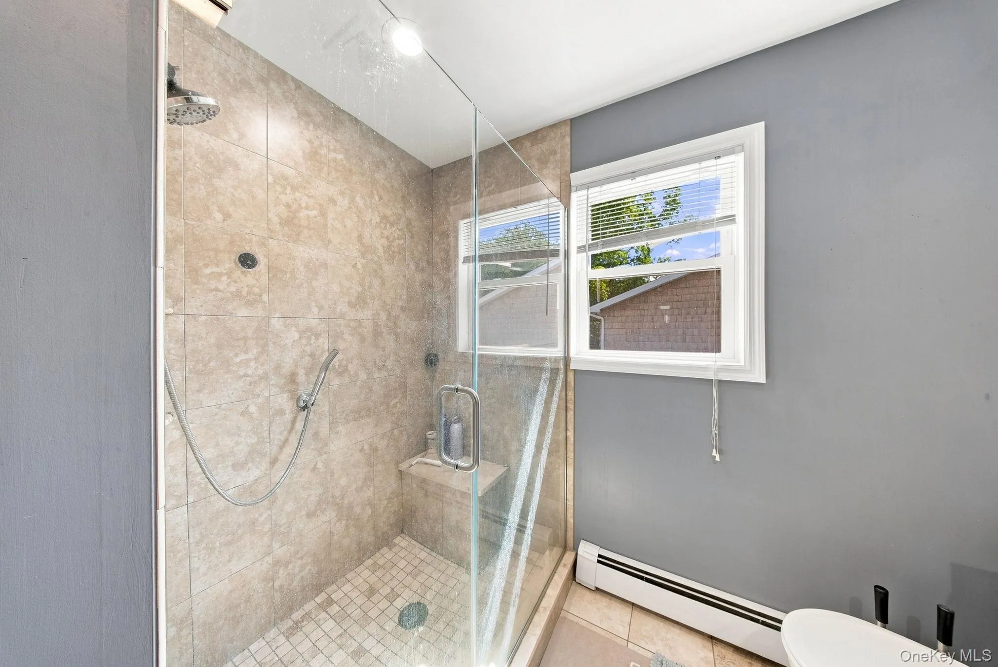 Tiled walk-in shower with glass enclosure, integrated shower bench, and a rainfall showerhead Tiled walk-in shower with glass enclosure, integrated shower bench, and a rainfall showerhead