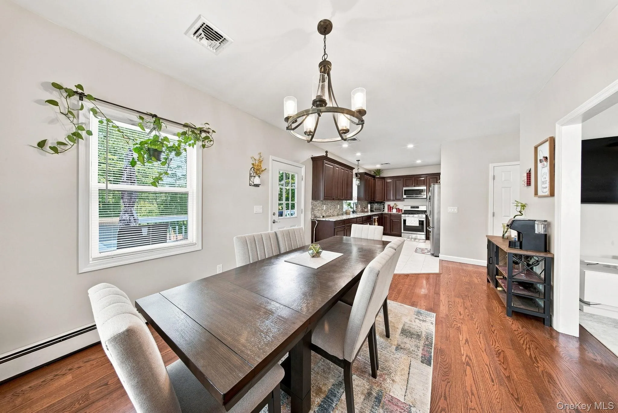 Open dining area showcasing rich wood-finish flooring, a dark wood dining table with seating for six, and a brushed metal chandelier Open dining area showcasing rich wood-finish flooring, a dark wood dining table with seating for six, and a brushed metal chandelier